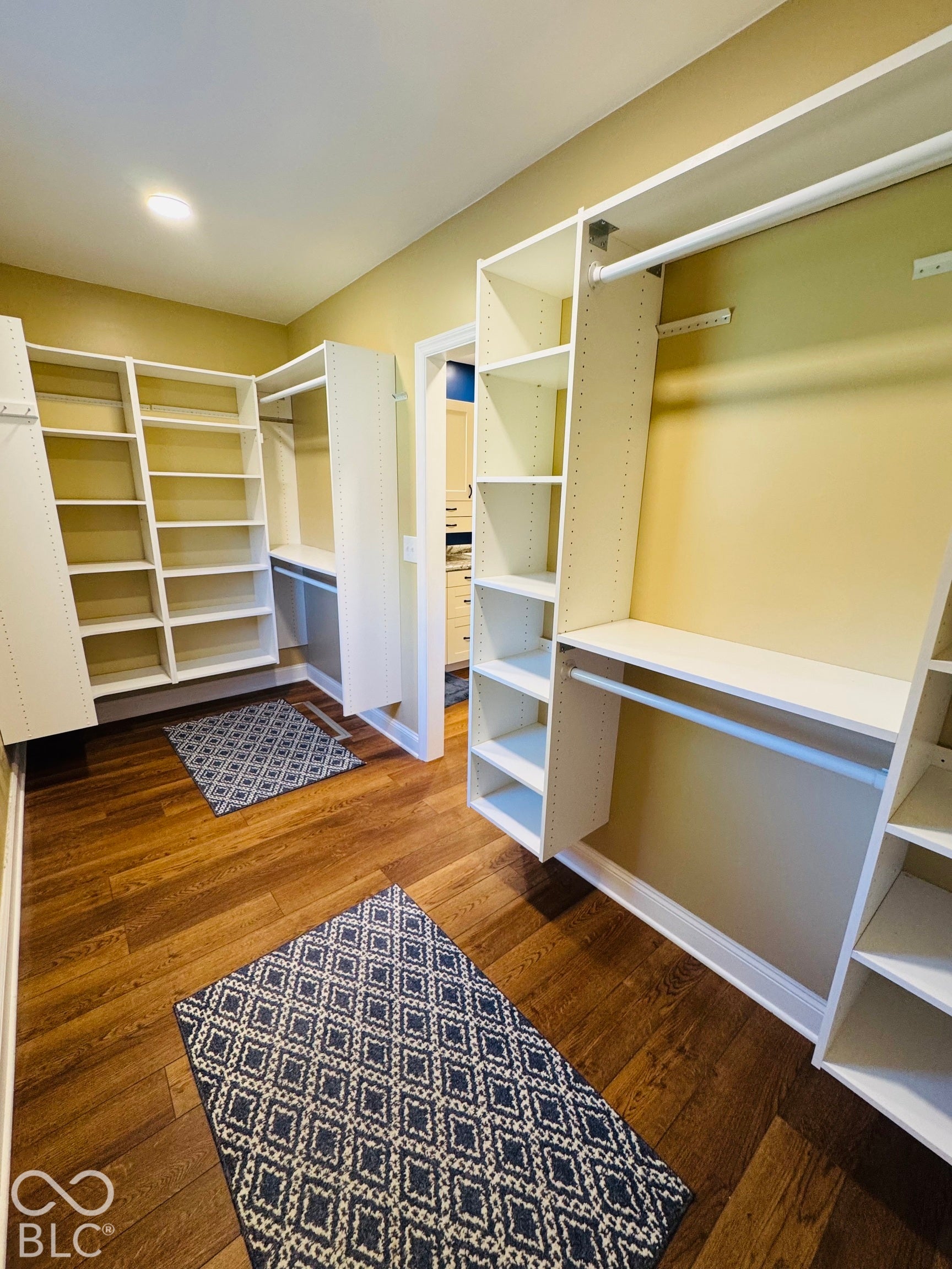 Wood-finish flooring, recessed lighting, and built-in closet systems with shelving and hanging rods