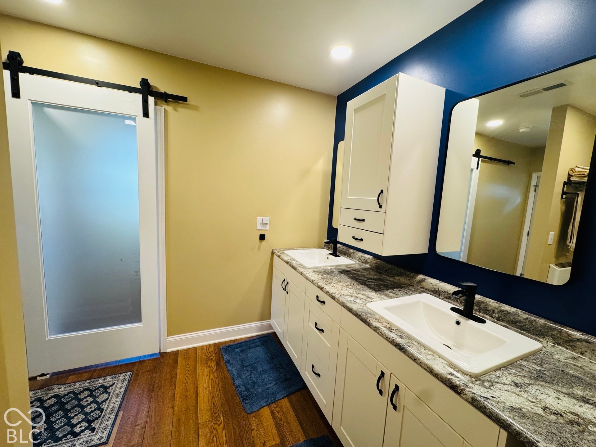 Double vanity with undermount sinks, wood-finish flooring, and a frosted glass barn door