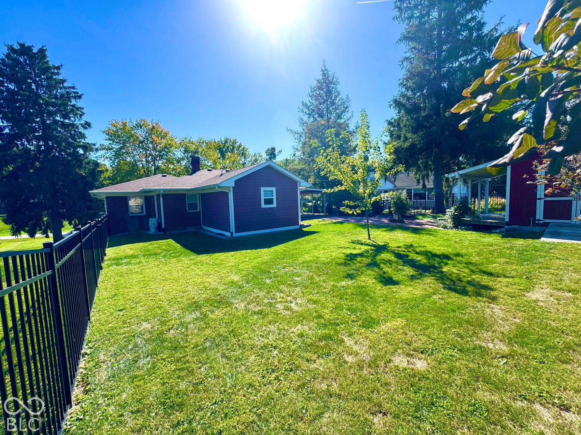 Fenced backyard featuring a manicured lawn, established landscaping, and a red-sided structure with a covered patio