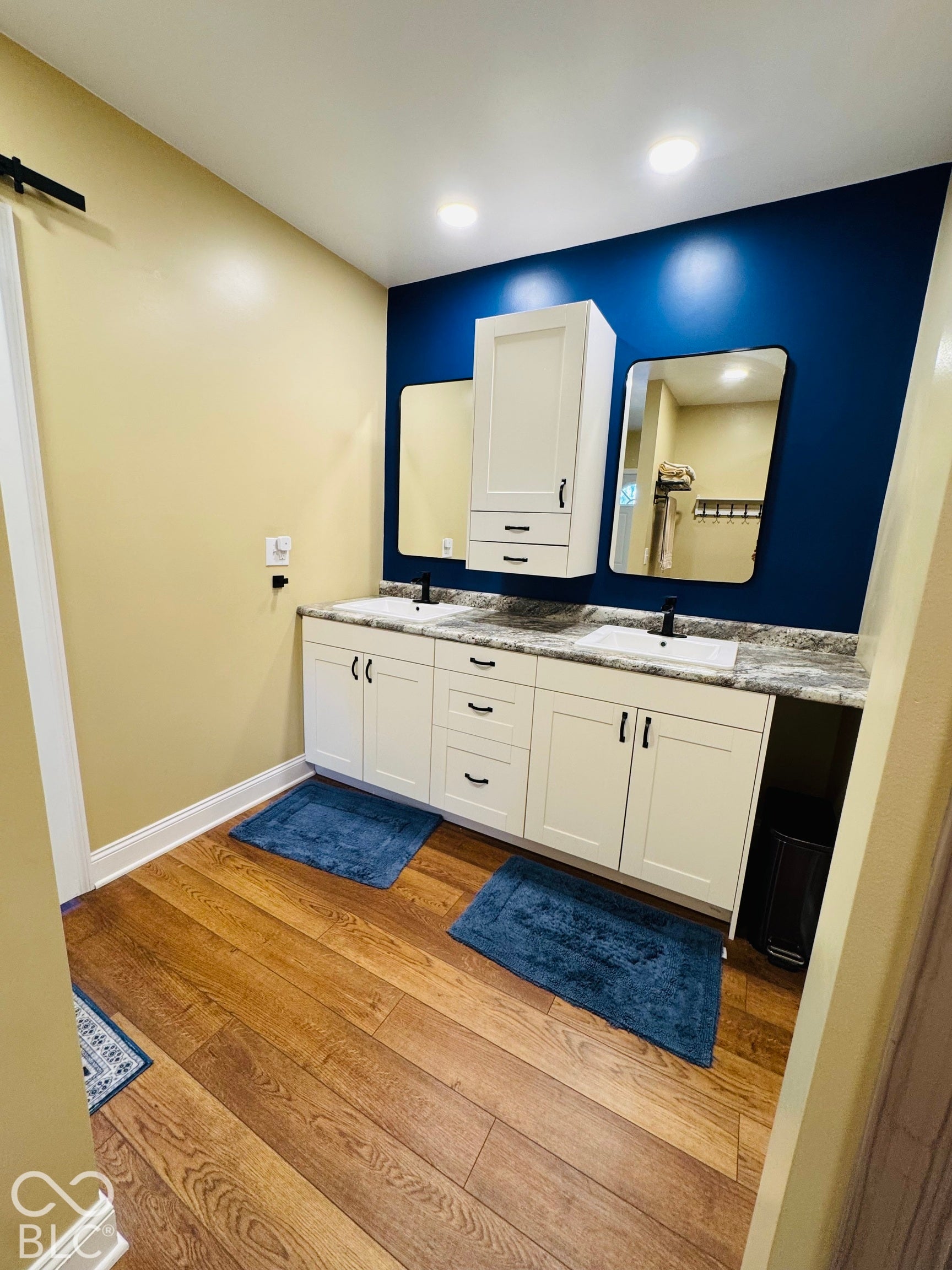 Dual vanity with white cabinetry, wood-finish flooring, recessed lighting, and a barn door hardware element