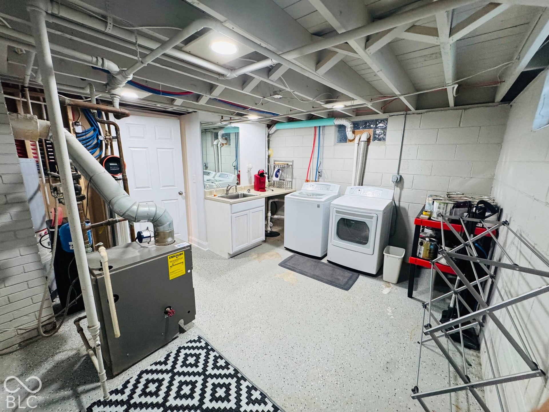 Utility area featuring a laundry sink, white cabinetry, a washer and dryer, and exposed ceiling joists