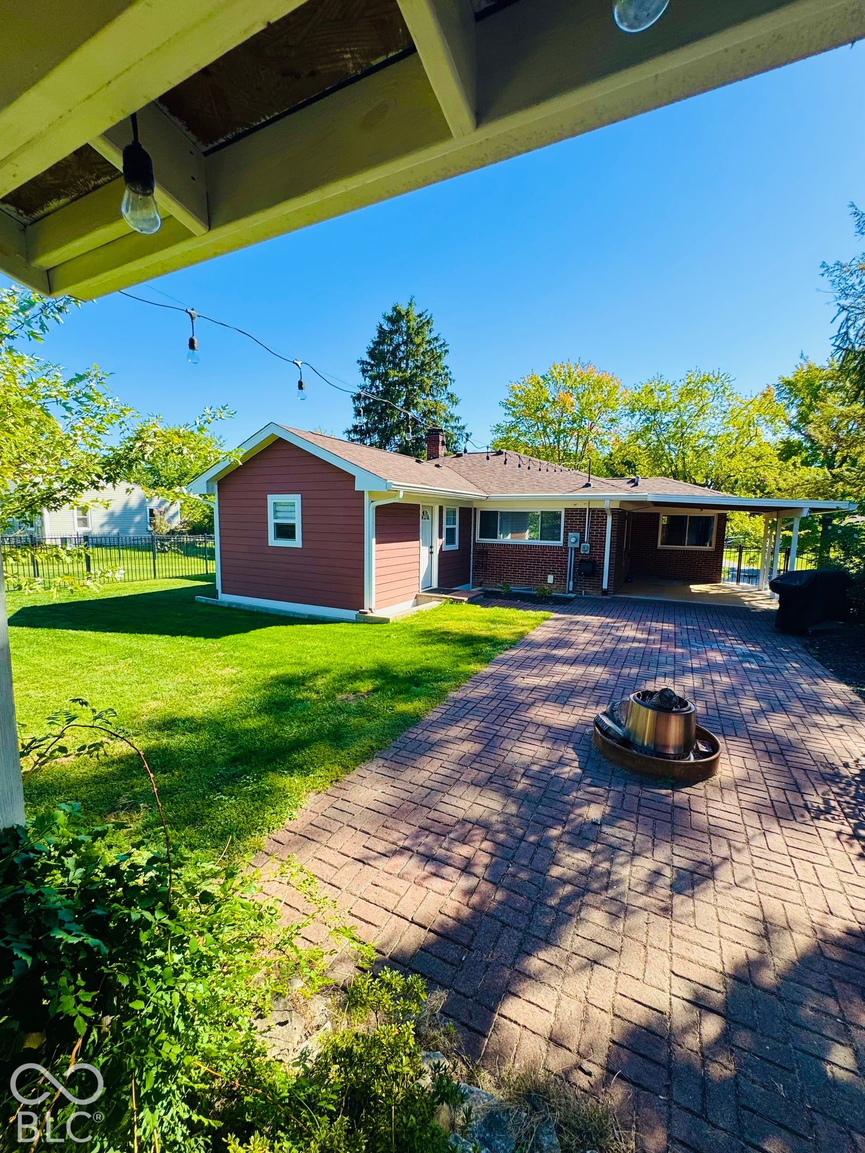 Expansive brick paver patio with a covered section, mature trees, and a well-maintained lawn