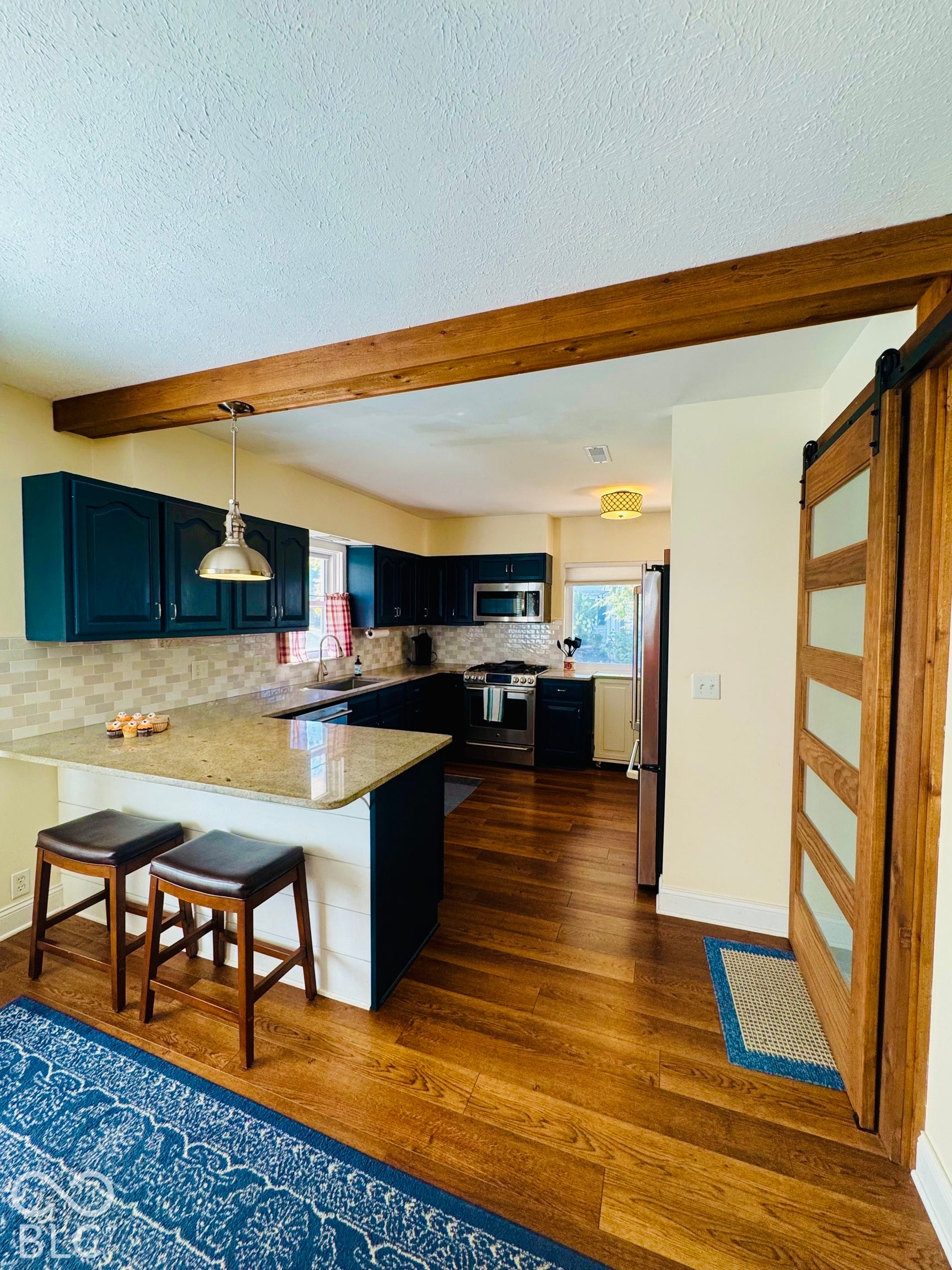 Open-concept kitchen with wood-finish flooring, dark cabinetry, and light-toned countertops and breakfast bar