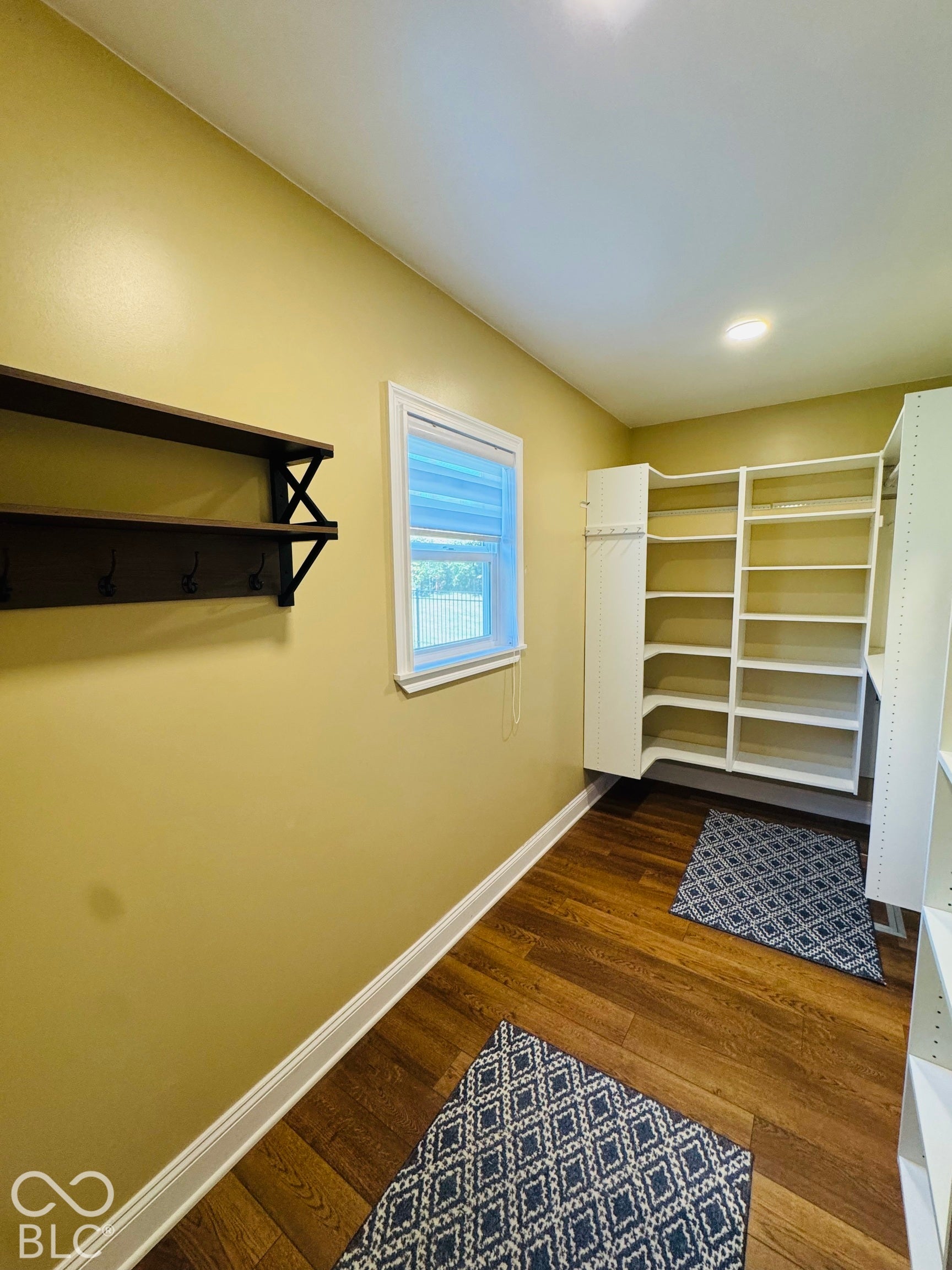 Wall-mounted shelving with integrated hooks, wood-finish flooring, recessed lighting, and built-in white shelving units