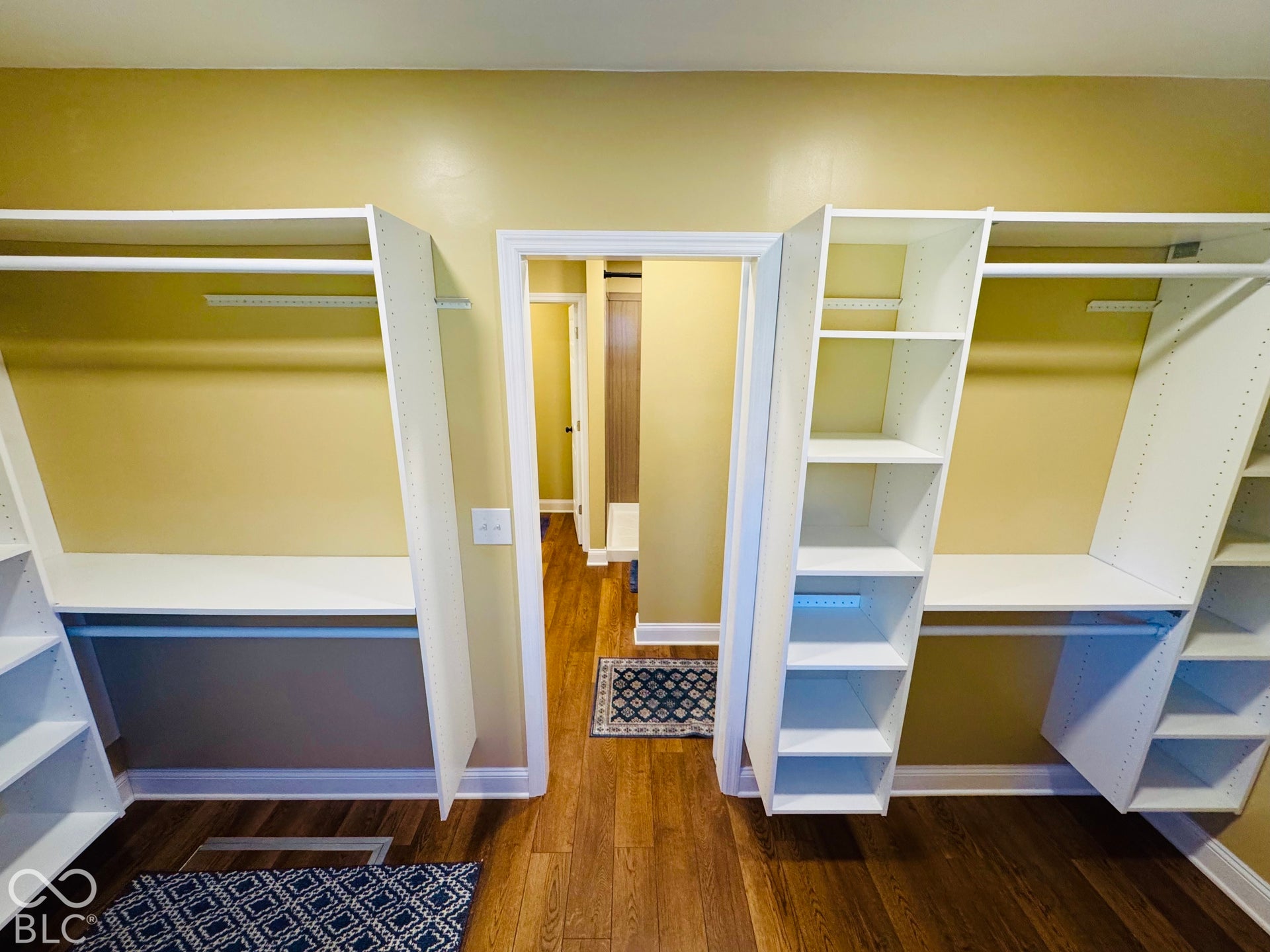 Primary Bedroom walk in closet with Built-in white shelving and hanging rods, wood-finish flooring, and light-toned wall paint