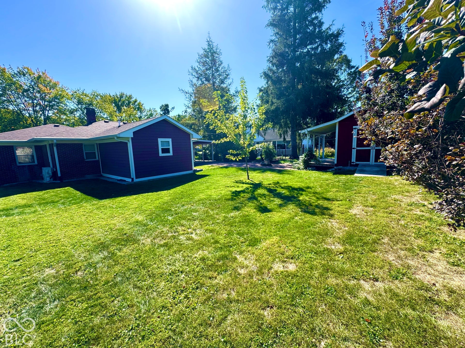 Expansive green space with a red siding outbuilding and mature trees