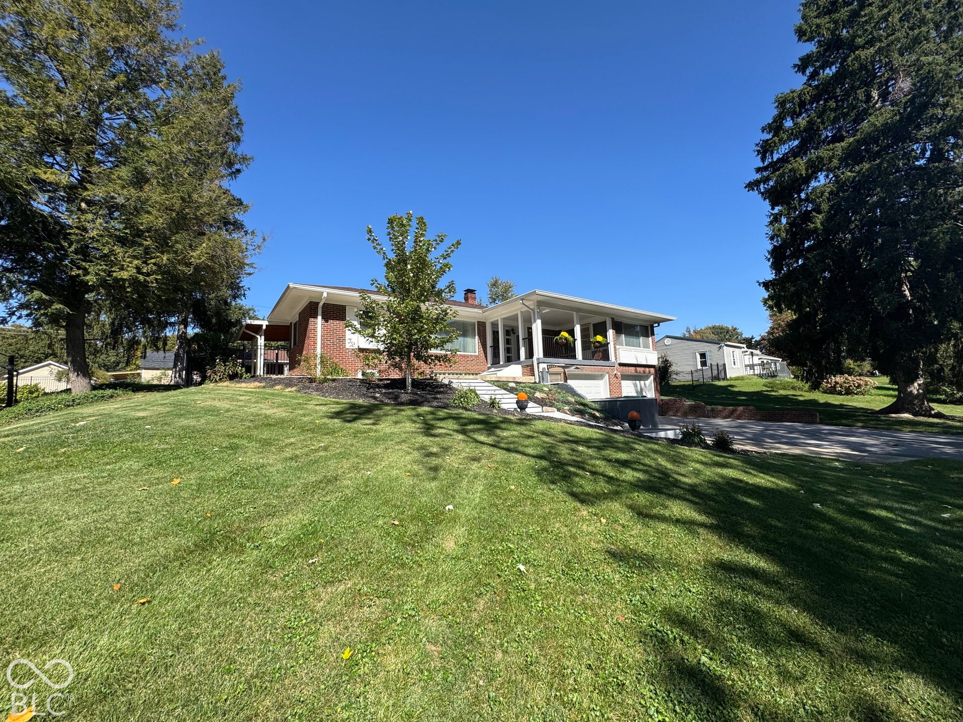 Brick  exterior with a covered front porch, integrated garage, and mature trees