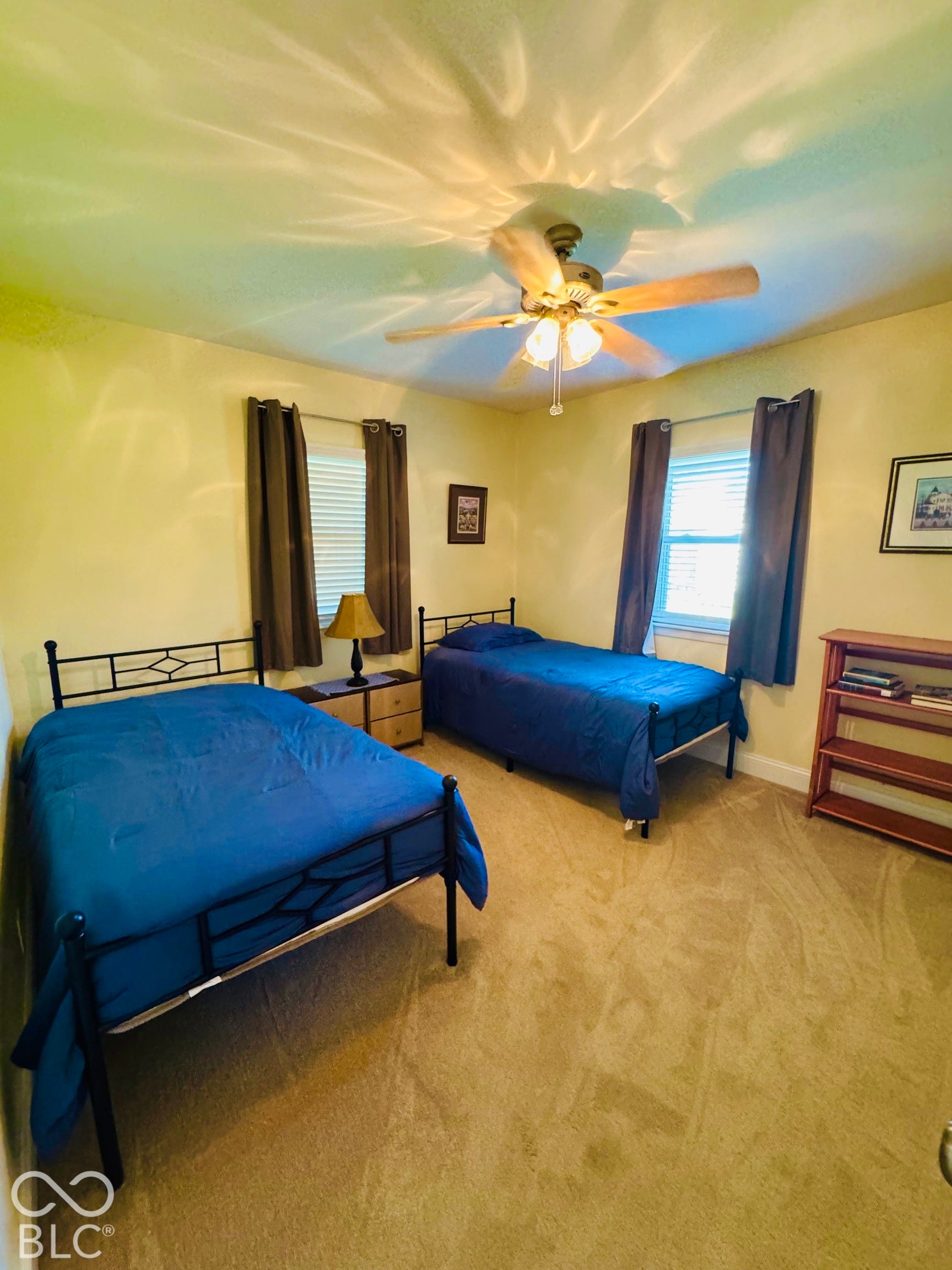 Carpeted room featuring a ceiling fan with light fixture and two windows with blinds