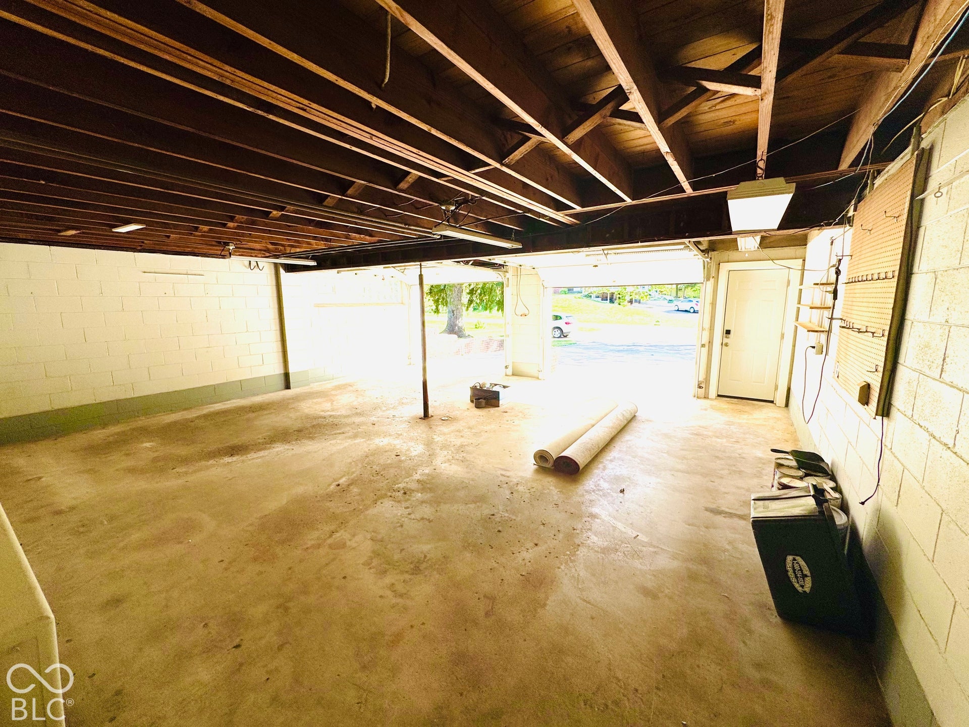 Exposed wood ceiling beams, concrete flooring, painted cinder block walls, overhead lighting fixtures, and a white entry door