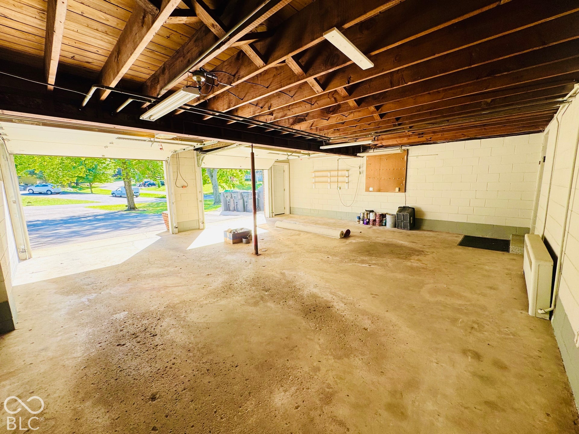 Finished and Heated garage featuring Concrete flooring, exposed wood beam ceiling, white painted block walls, two insulated overhead garage doors, interior fluorescent lighting