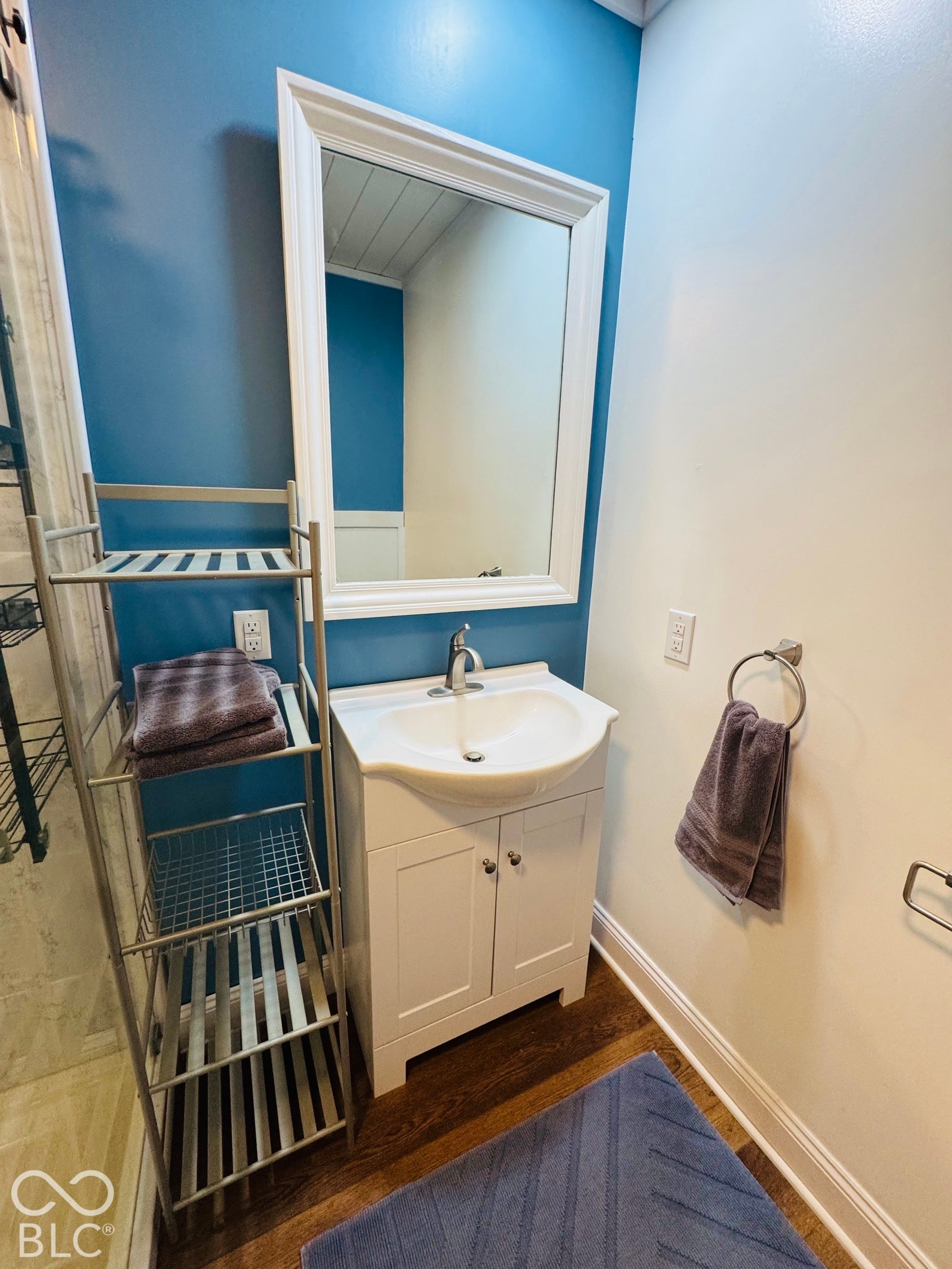 White framed wall mirror, single vanity with integrated sink, chrome faucet, wood-finish flooring, and two-tone wall treatment