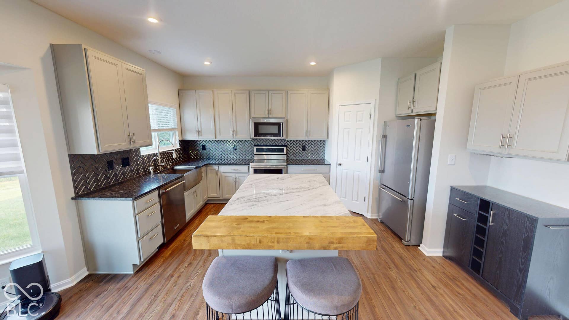 Spacious kitchen featuring wood-finish flooring, white cabinetry, dark countertops, a dark tile backsplash, and stainless steel appliances