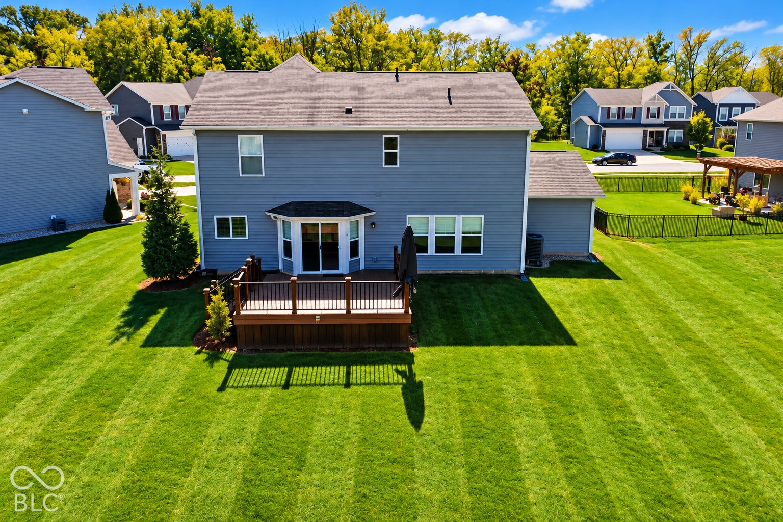 *AI - Color Enhancement* Expansive lawn with a two-story residence featuring blue siding, a dark roof, and a ground-level deck with white railings