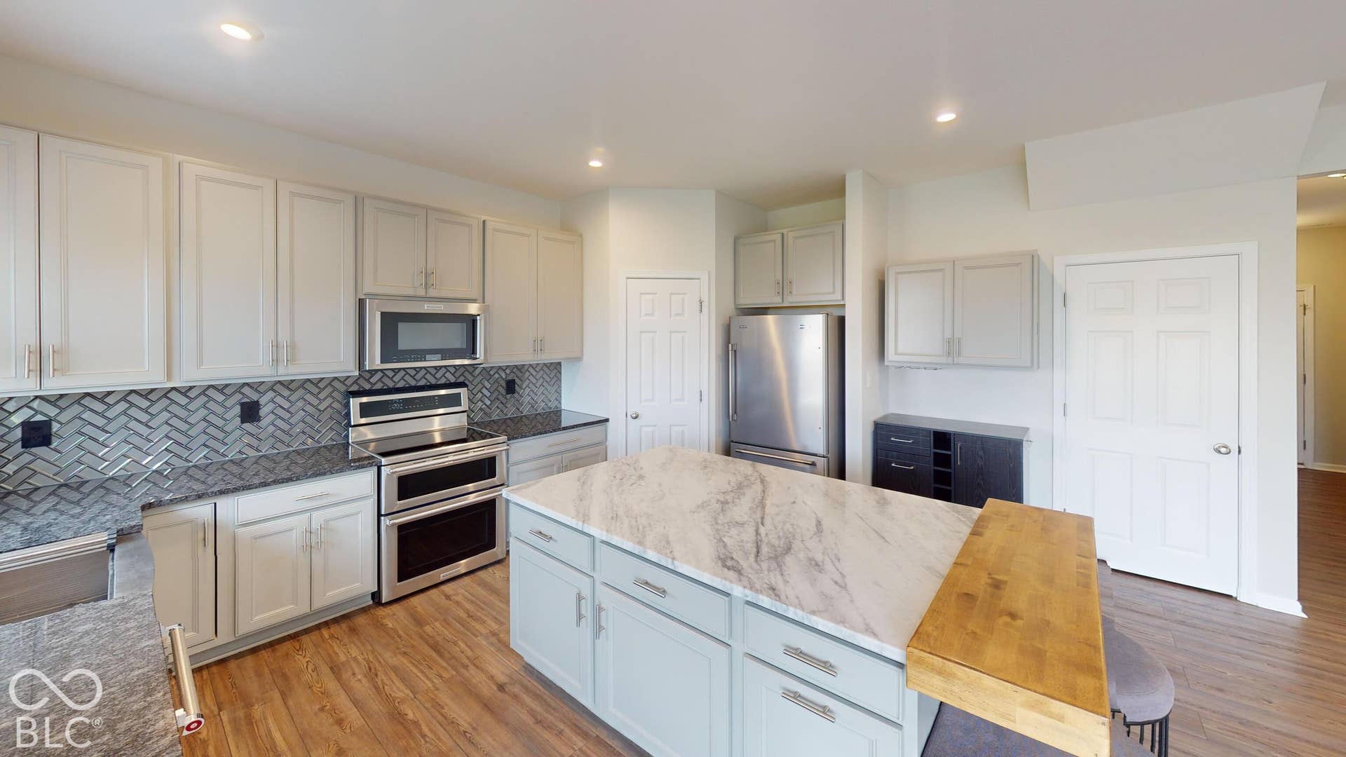 Kitchen featuring light-toned cabinetry, stainless steel appliances, herringbone pattern tile backsplash, and a large center island with a stone-finish countertop