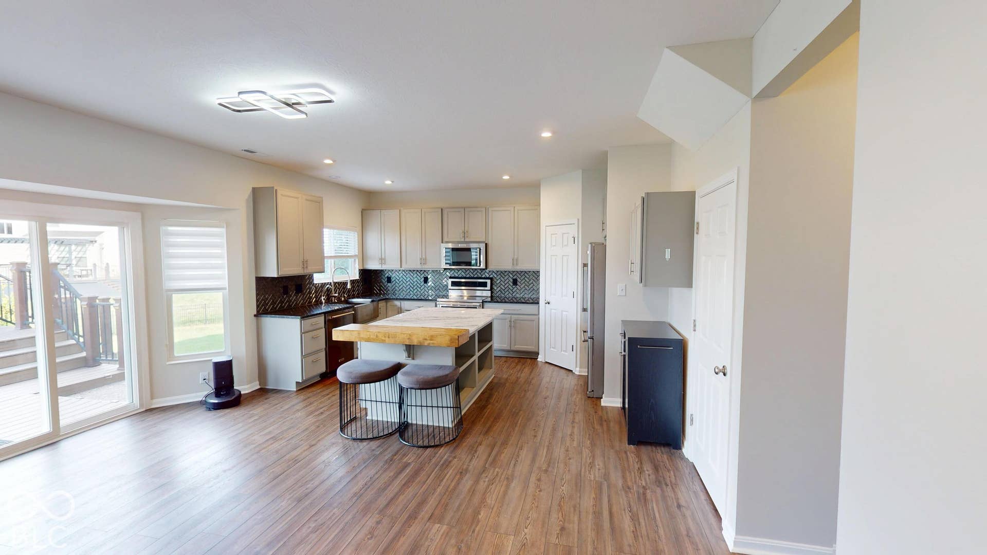 Open-concept living area featuring wood-finish flooring, a contemporary ceiling light fixture, sliding glass doors to the exterior deck, a kitchen island with a butcher block top, and a mosaic tile backsplash
