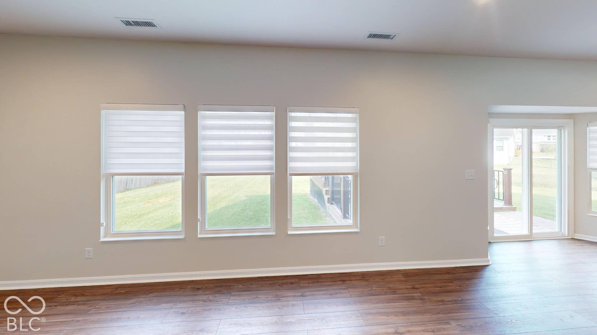 Wood-finish flooring with white baseboards, multiple windows featuring privacy blinds, and a sliding glass door providing access to an outdoor patio