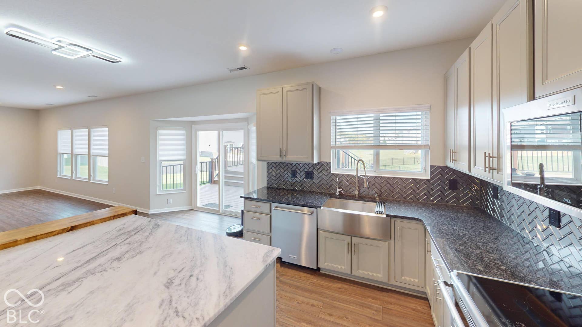 Kitchen featuring light-toned cabinetry, stainless steel appliances, dark countertop, and herringbone tile backsplash