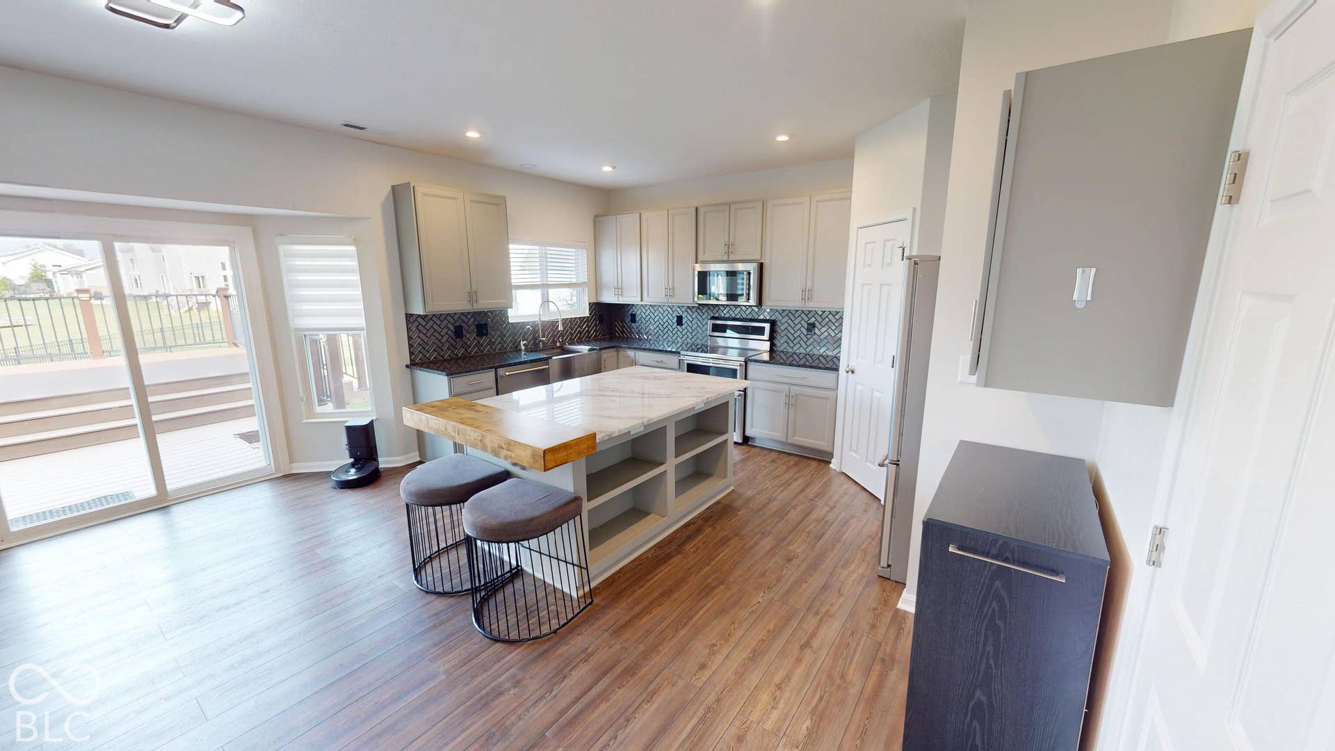 Wood-finish flooring, sliding glass patio door, light gray cabinetry, stainless steel appliances, and a kitchen island with a light-toned countertop