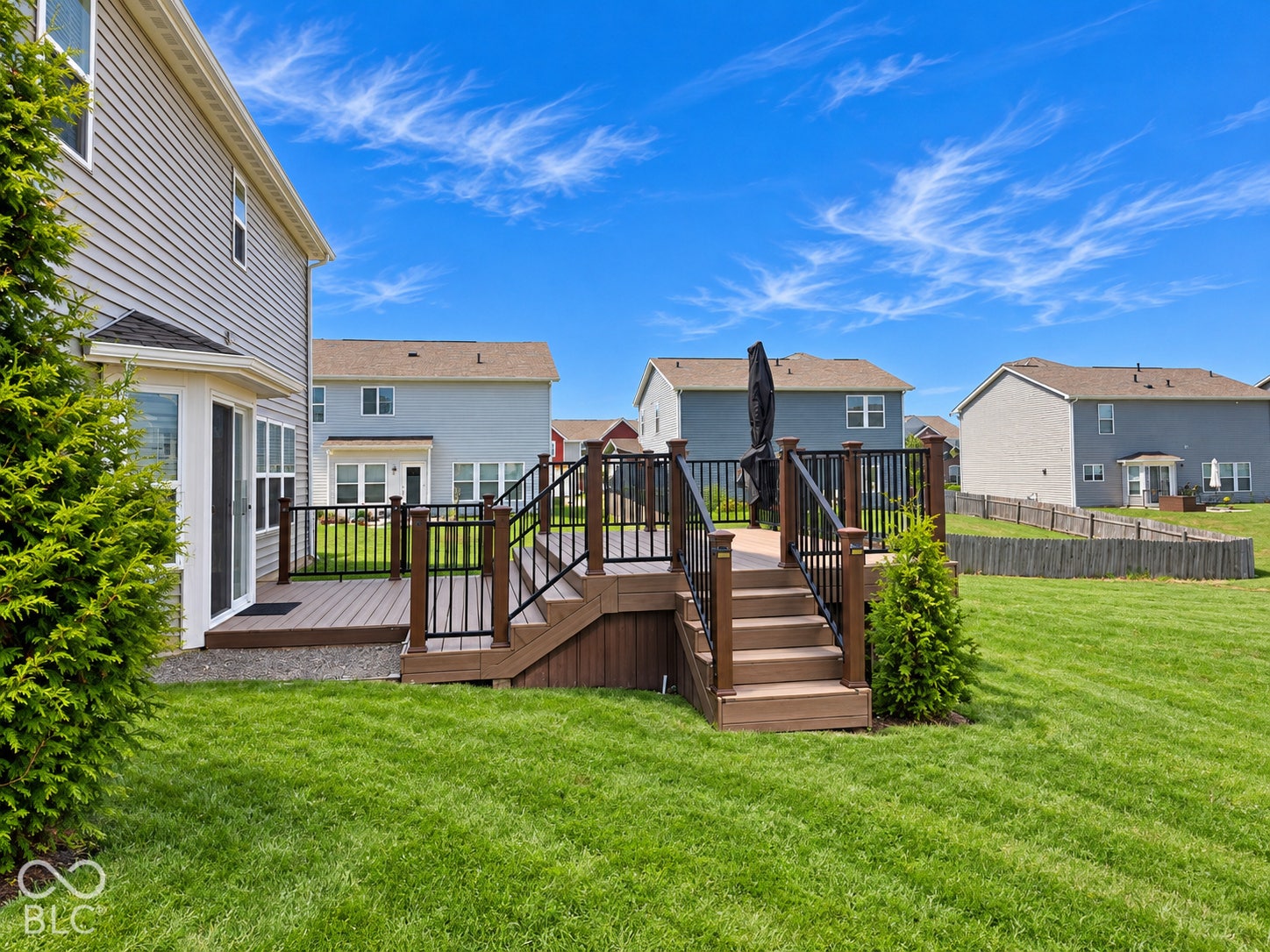 *AI - Color Enhancement* Expansive backyard featuring a manicured lawn, multi-level composite deck, and black metal railings with wooden newel posts