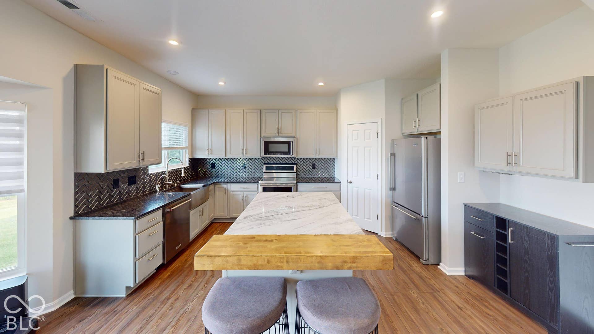 Modern kitchen featuring light cabinetry, stainless steel appliances, dark countertops with a geometric backsplash, and a large central island with a wood-finish breakfast bar