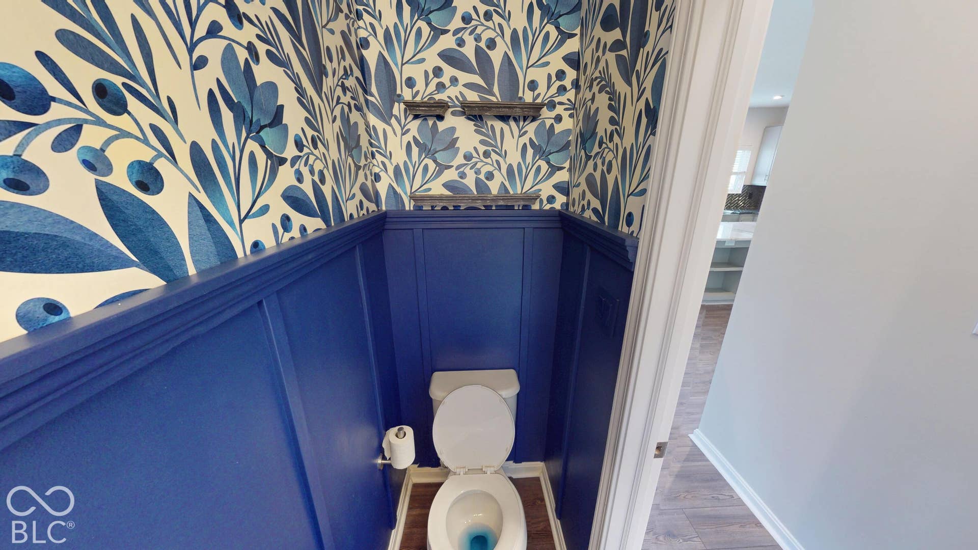 Patterned wallpaper, wood-finish flooring, wainscoting, and accent shelving | Half Bathroom