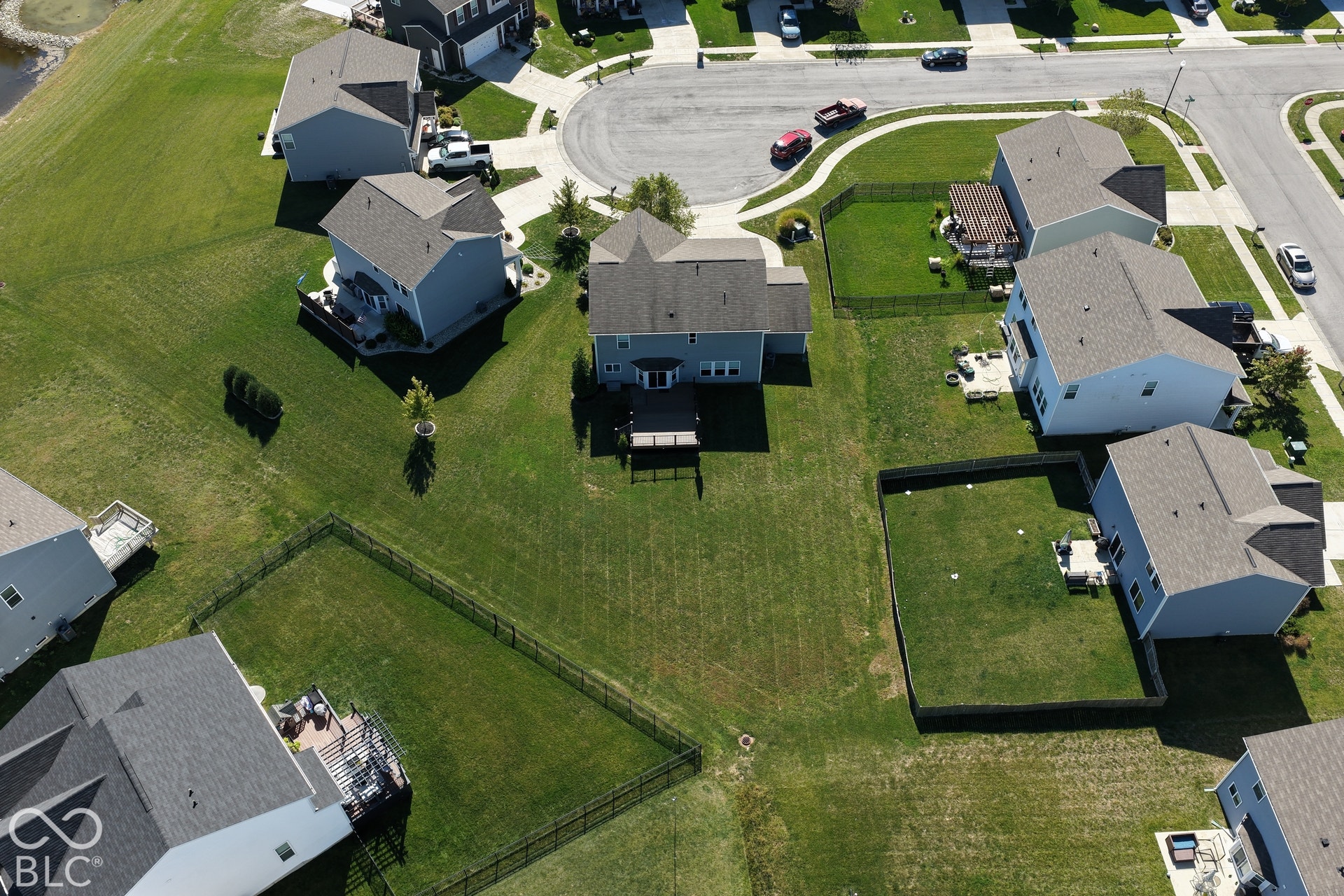 *Unaltered Exterior Stills* Expansive green lot with established perimeter fencing, featuring a multi-level deck and a paved residential street