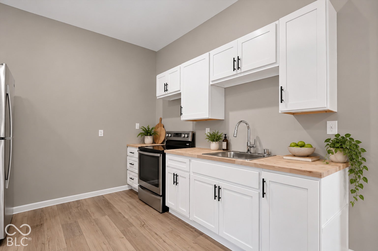 Kitchen featuring white shaker-style cabinetry, matte black hardware, butcher block countertops, stainless steel appliances, and wood-finish flooring