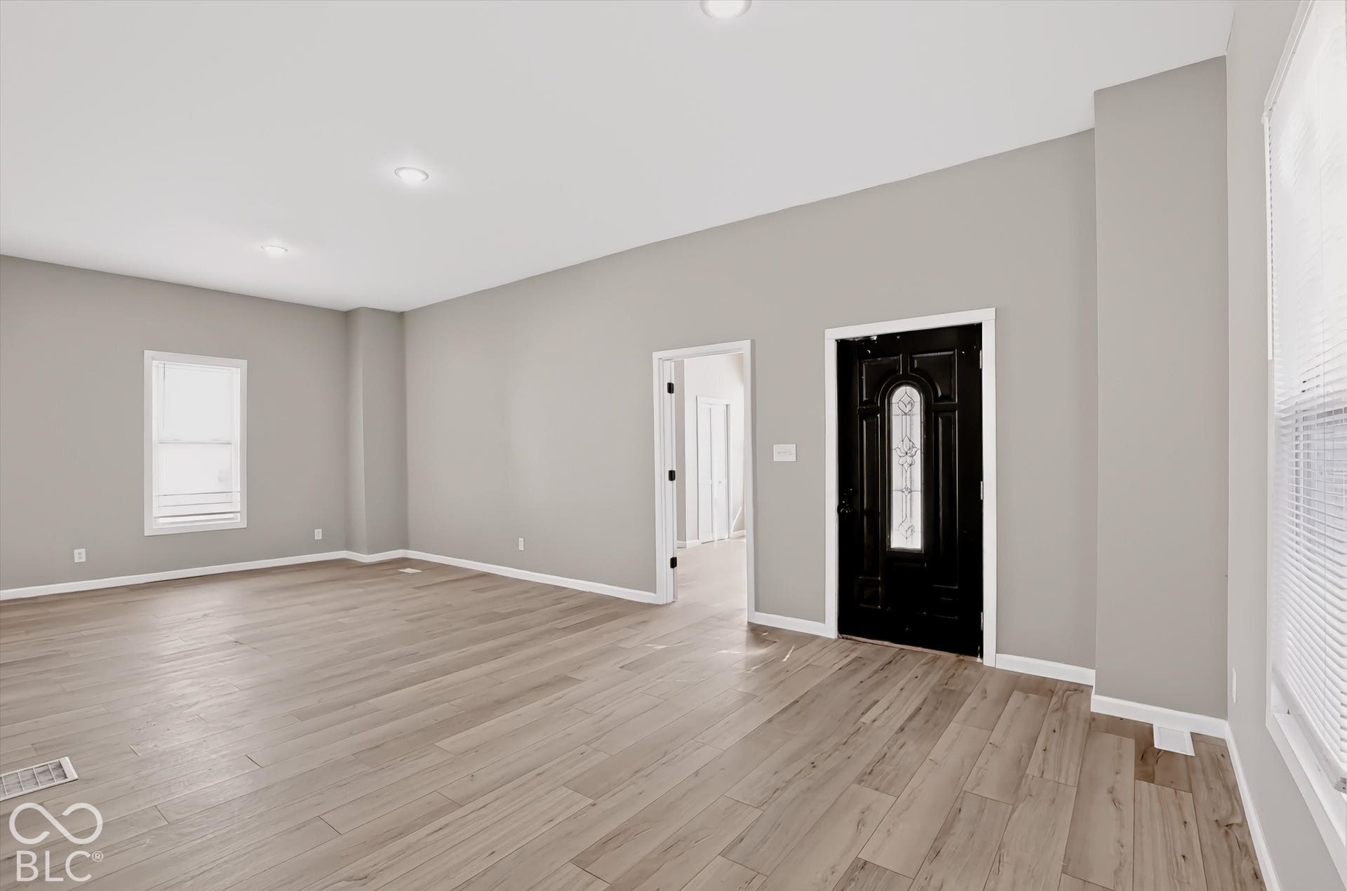 Neutral-toned interior featuring wood-finish flooring, recessed lighting, and a black front door with decorative glass insert