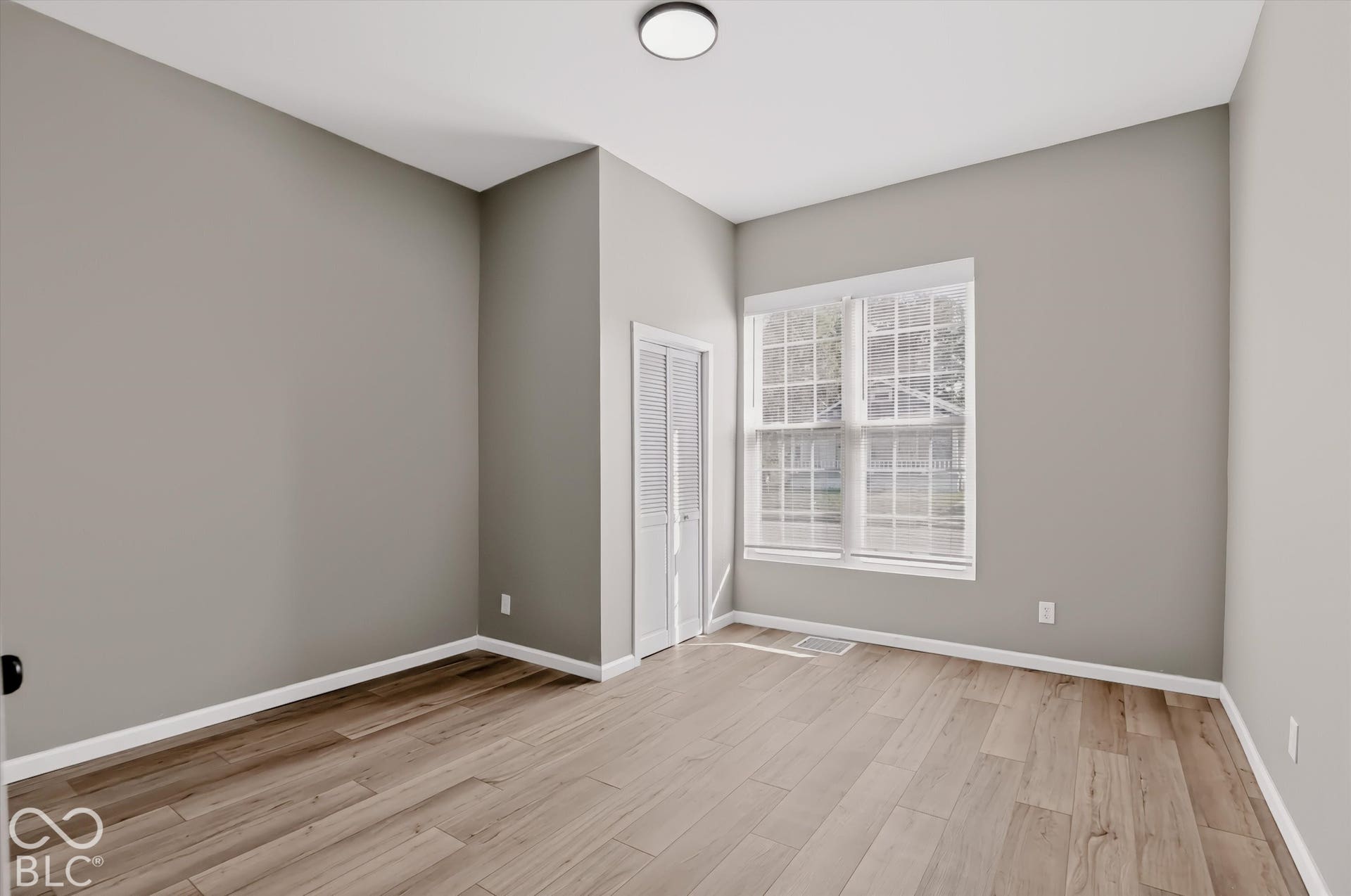 Neutral-toned walls, wood-finish flooring, multi-pane window with white trim, and white louvered closet doors