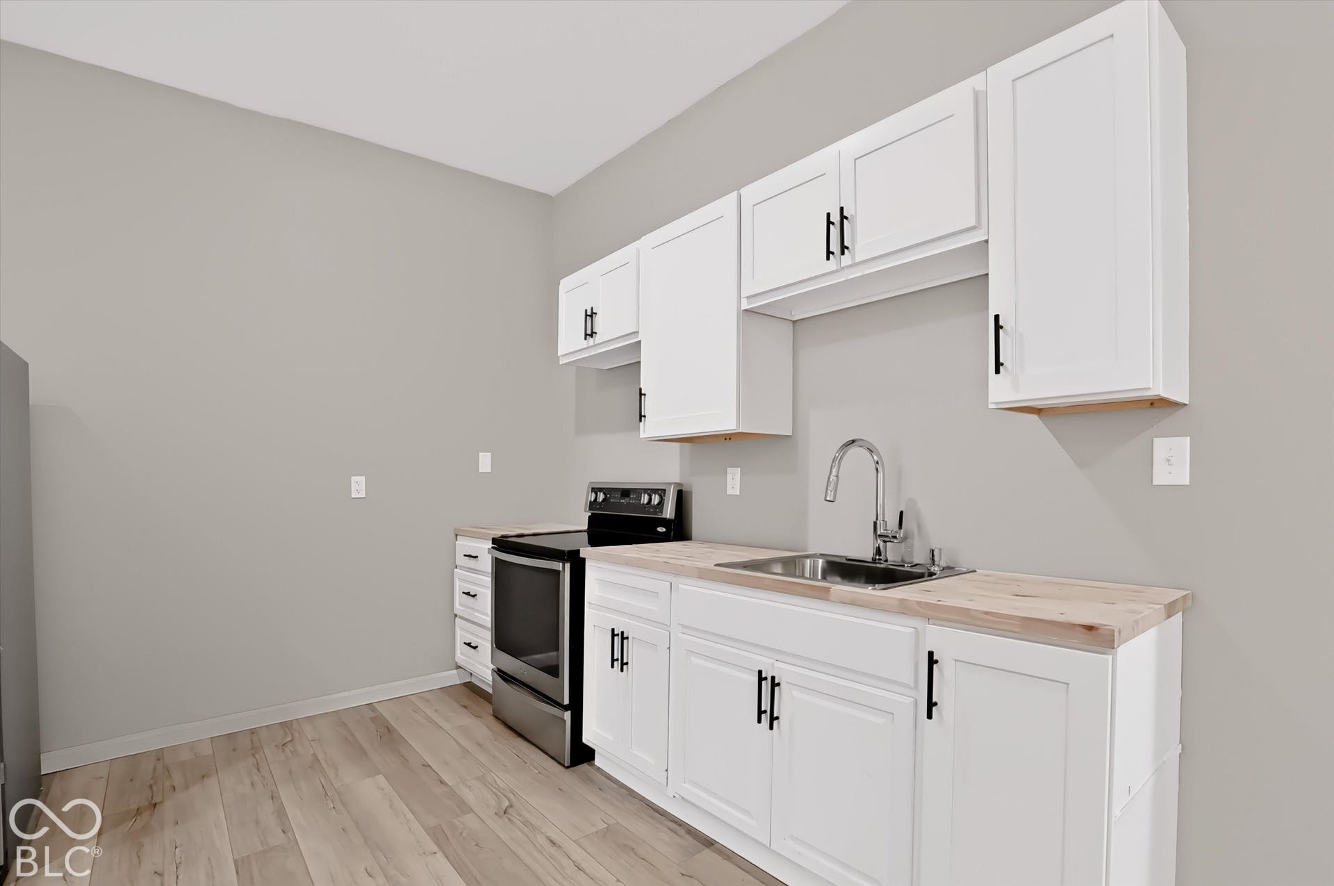 Virtually Altered - Kitchen featuring white shaker-style cabinetry, wood-finish countertops, stainless steel undermount sink with gooseneck faucet, integrated stainless steel range, and wood-finish flooring