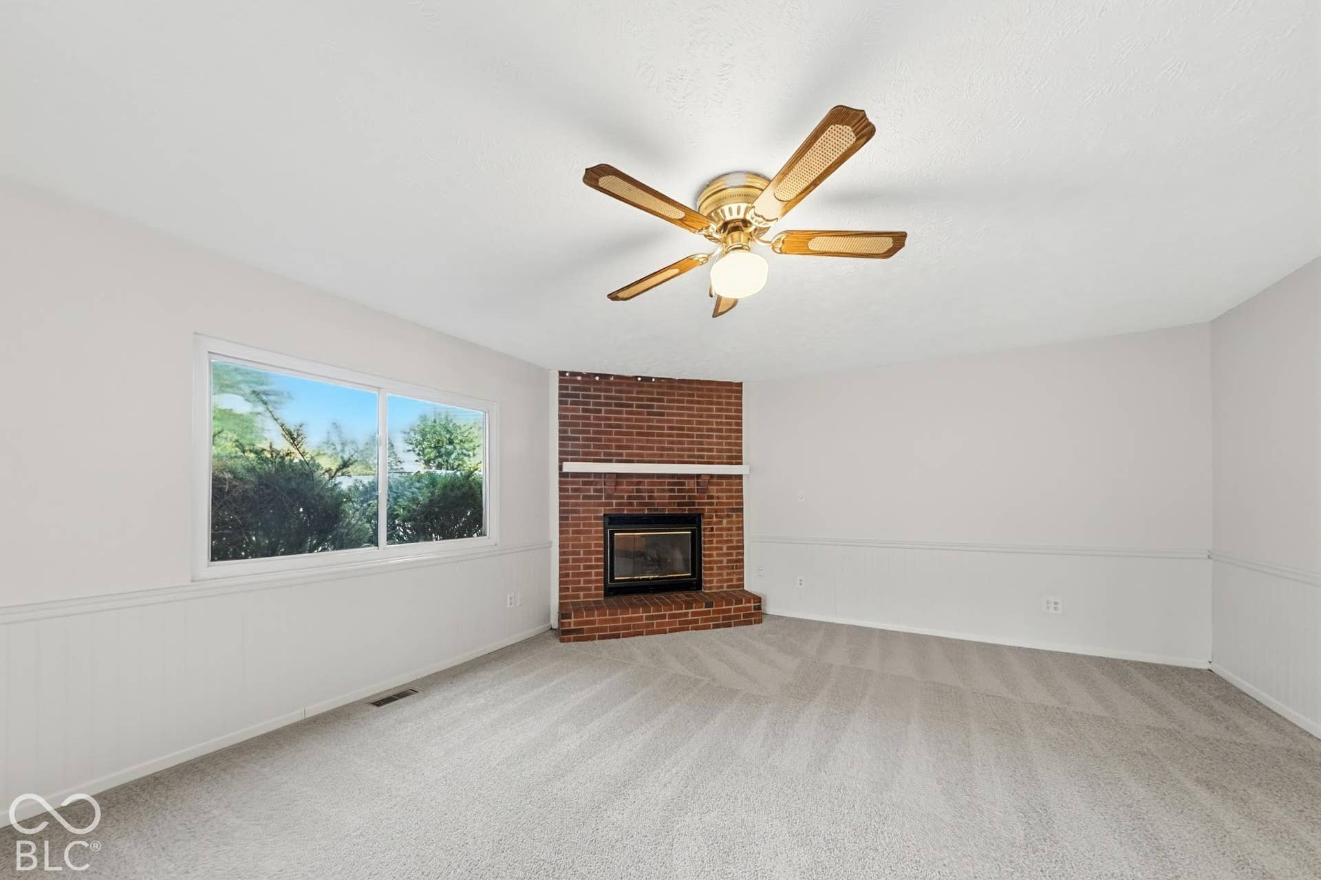 Window with natural light, brick fireplace, wall paneling, ceiling fan, and light-toned carpet