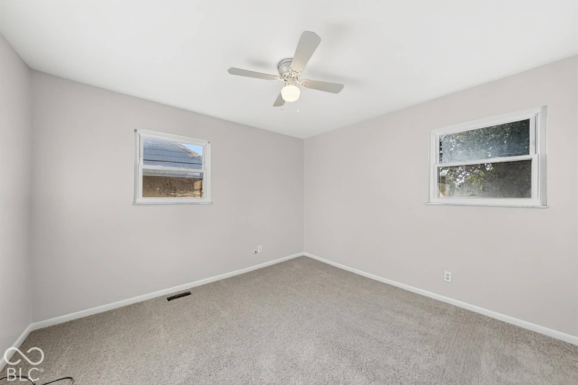 Neutral wall color, light gray carpeting, ceiling fan with integrated lighting, and two windows