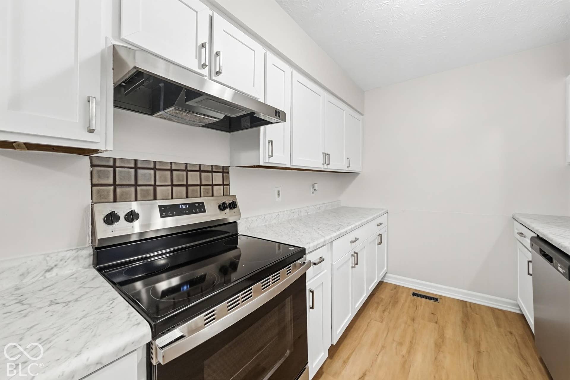 White cabinetry, light-toned countertops, stainless steel range with hood, patterned tile backsplash, and wood-finish flooring