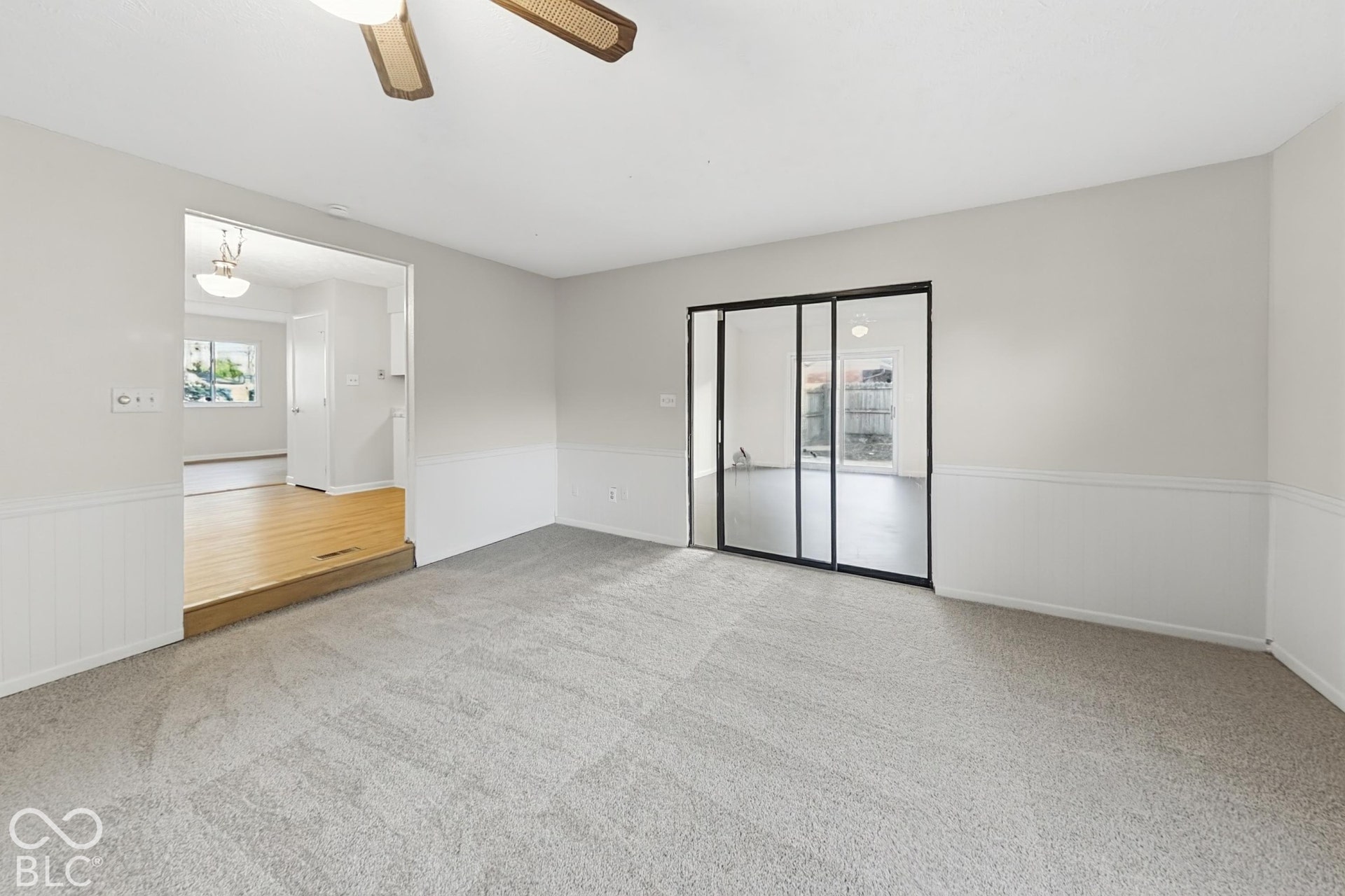 Neutral wall color, ceiling fan, carpet flooring, wainscoting, and sliding glass doors