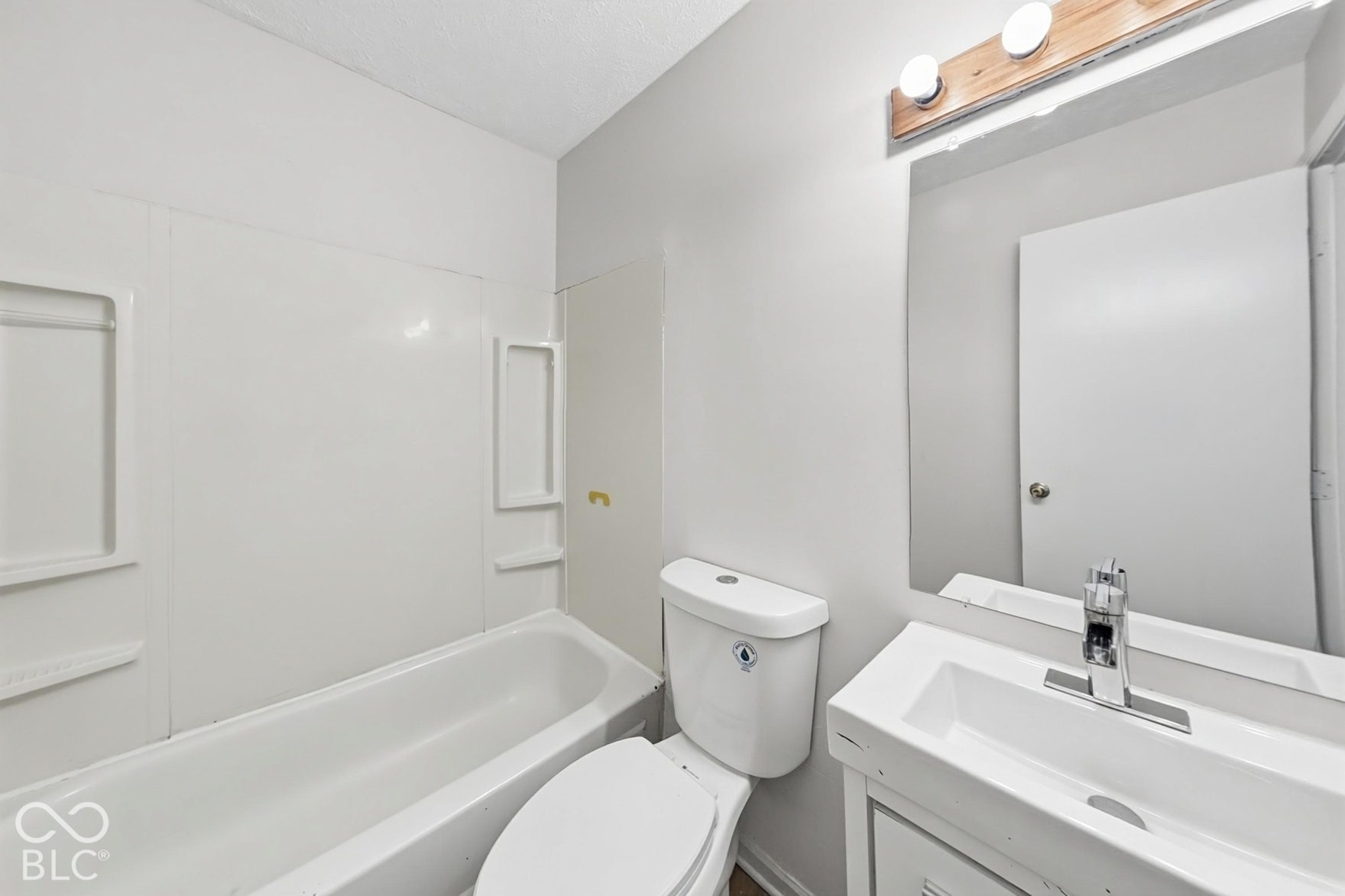 Bathtub with surround, toilet, vanity with integrated sink, and wall-mounted mirror