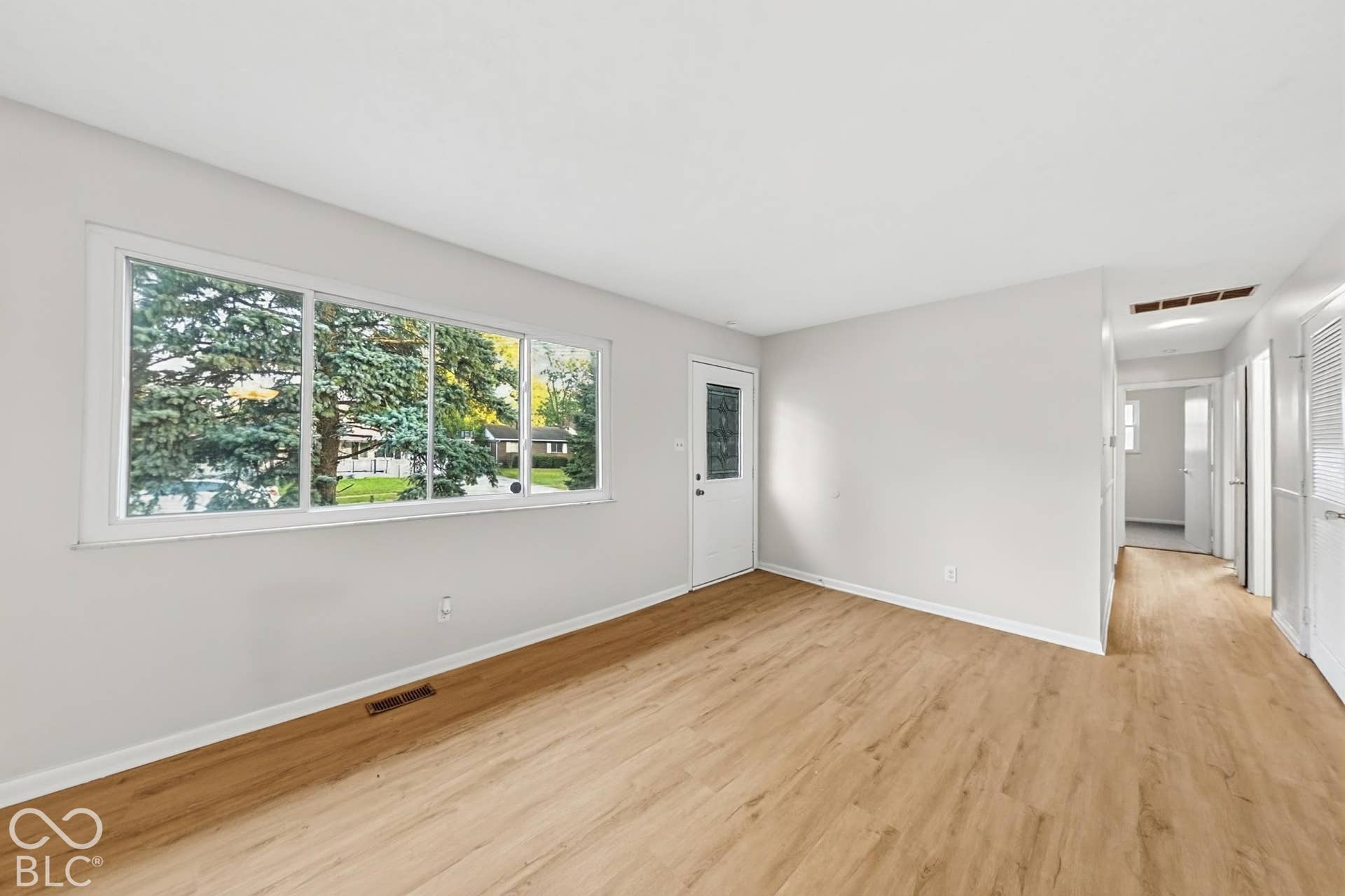 Expansive room featuring wood-finish flooring, a large multi-pane window, and a white entry door with decorative glass