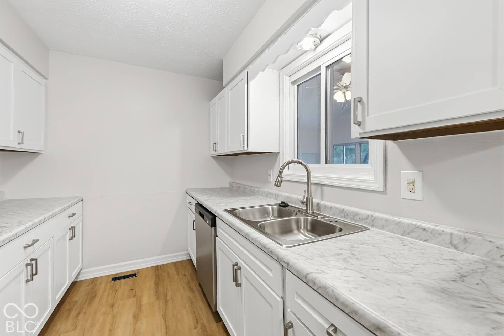 White cabinetry with brushed nickel hardware, light-toned countertops, stainless steel double basin sink, stainless steel dishwasher, and wood-finish flooring