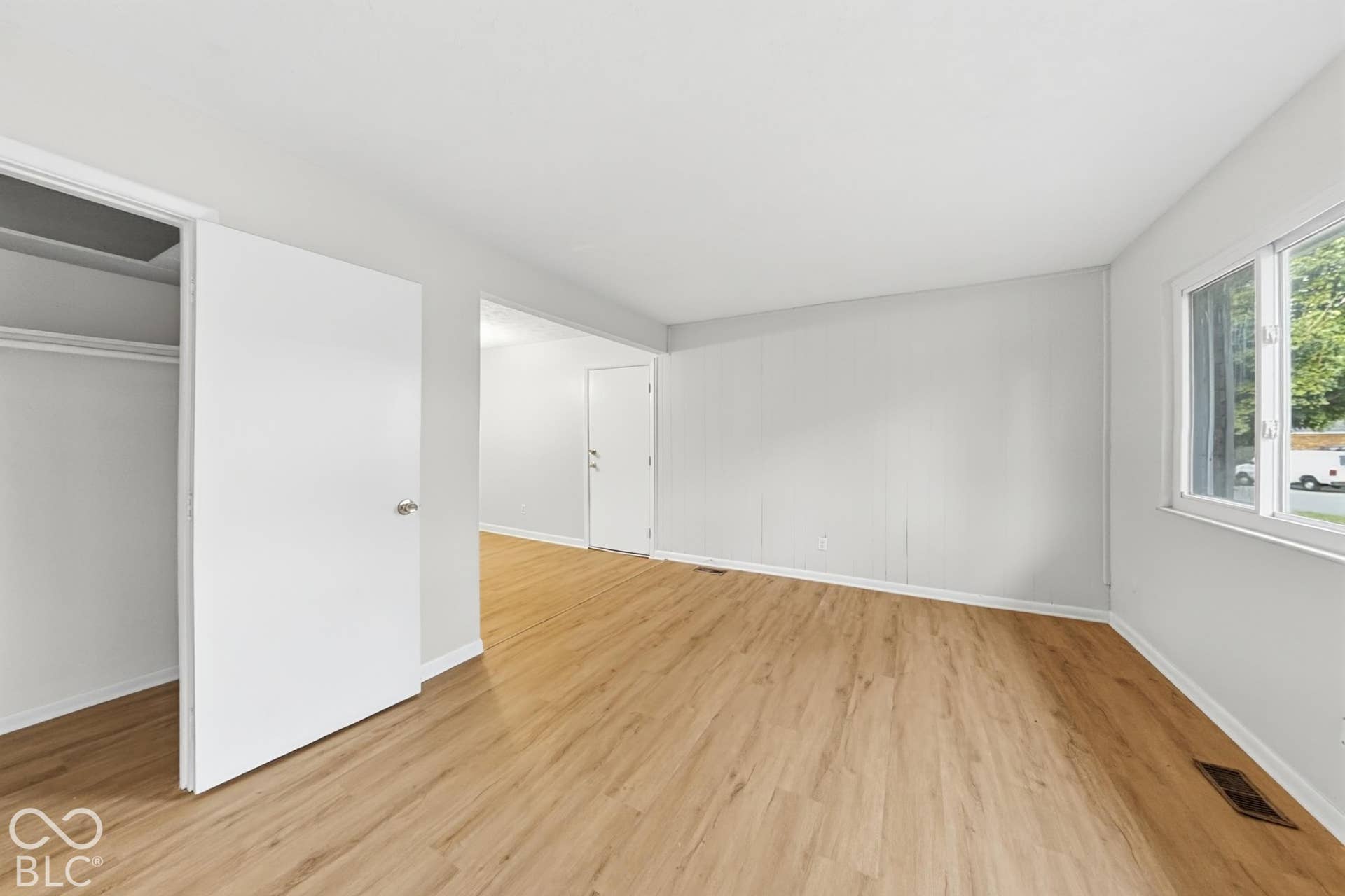 Light wood-finish flooring with white baseboards, a single window with white trim, and a built-in closet with a white door