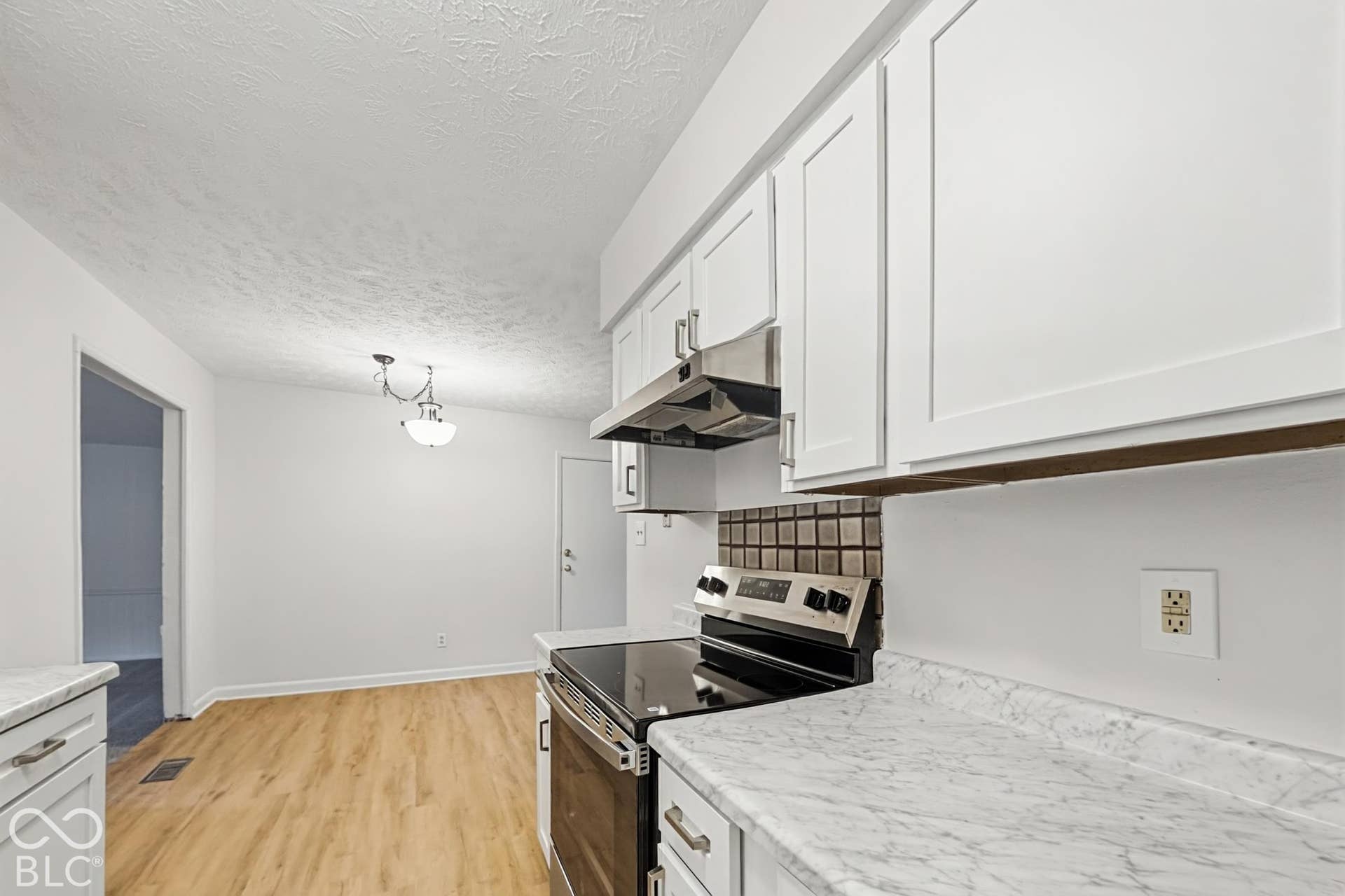 Kitchen featuring white shaker-style cabinetry, a stainless steel range and hood, mosaic tile backsplash, and light wood-finish flooring