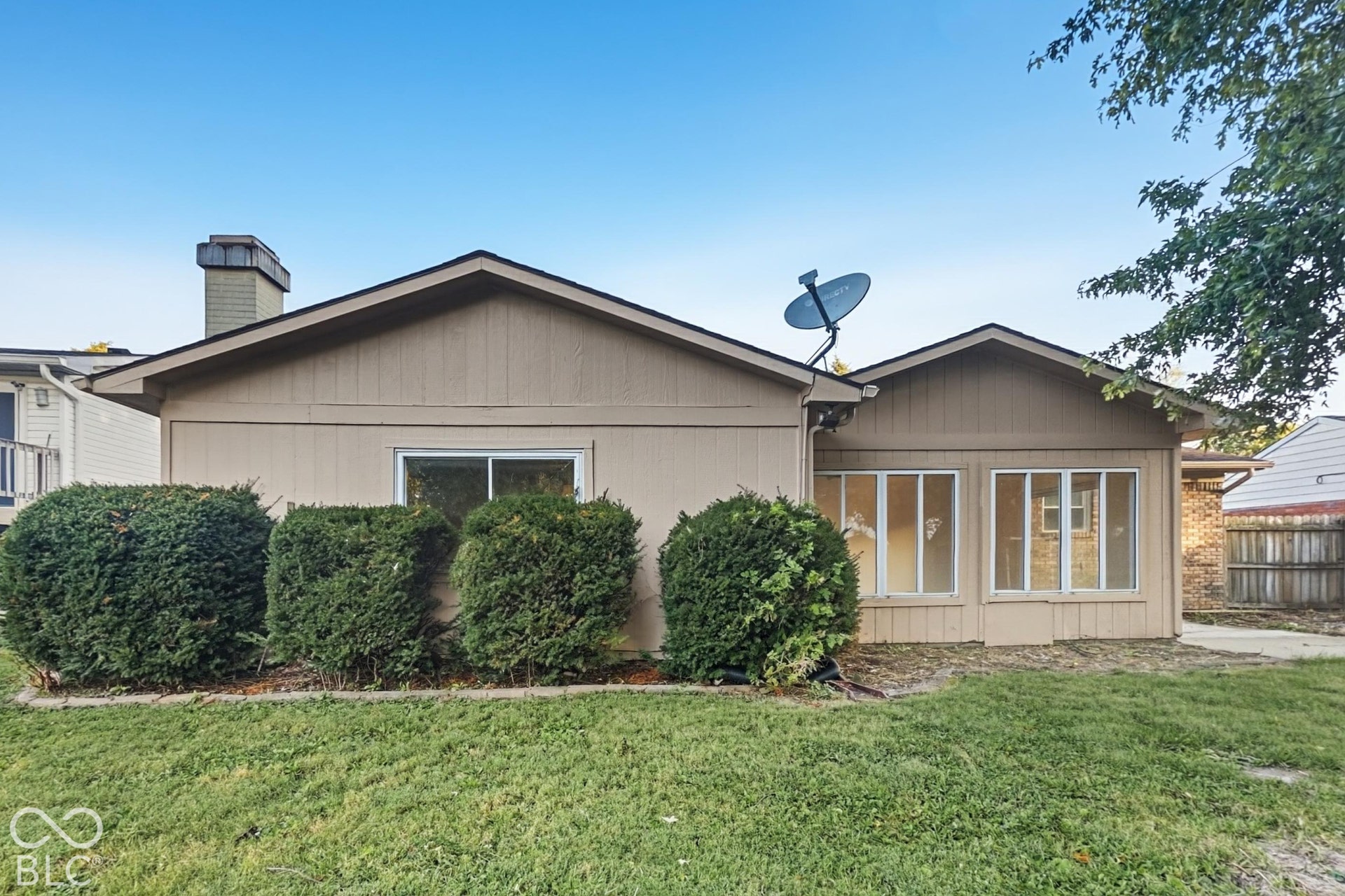 Gable roofline, rear-facing windows, chimney, sunroom addition, and mature landscaping
