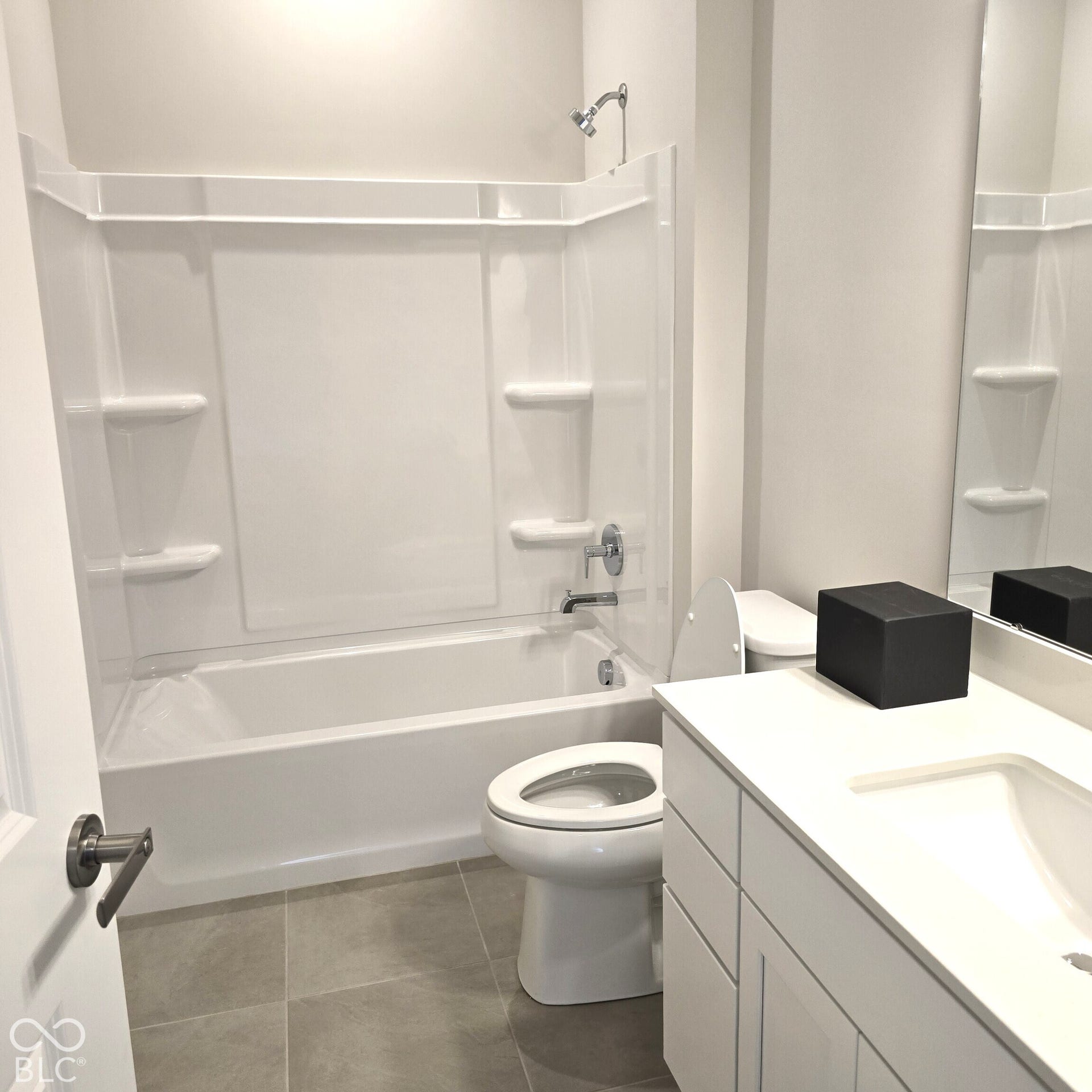 White bathtub with integrated shelving, chrome fixtures, white toilet, single vanity with integrated sink, and large wall mirror