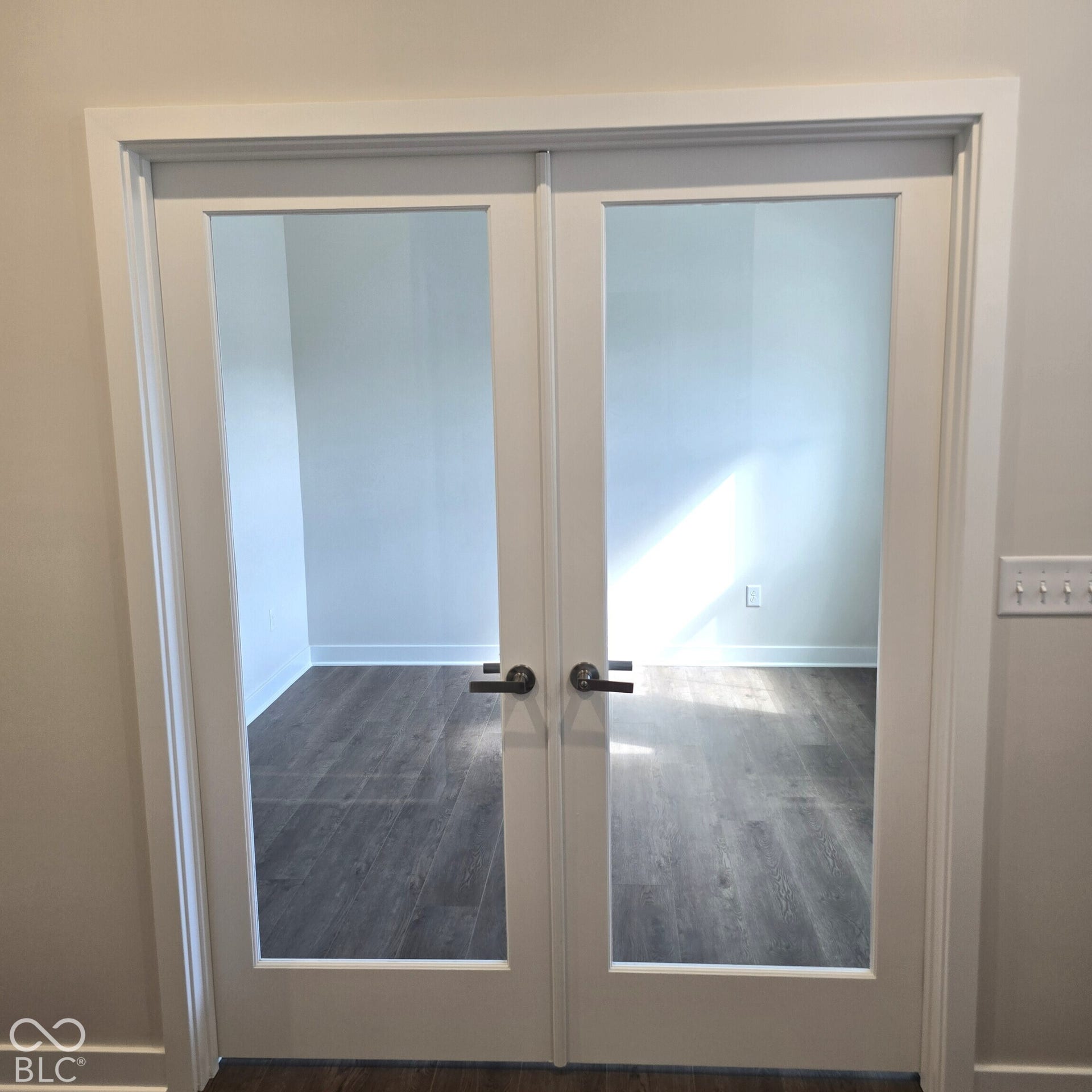 White French doors with clear glass panels, contrasting dark hardware, and wood-finish flooring