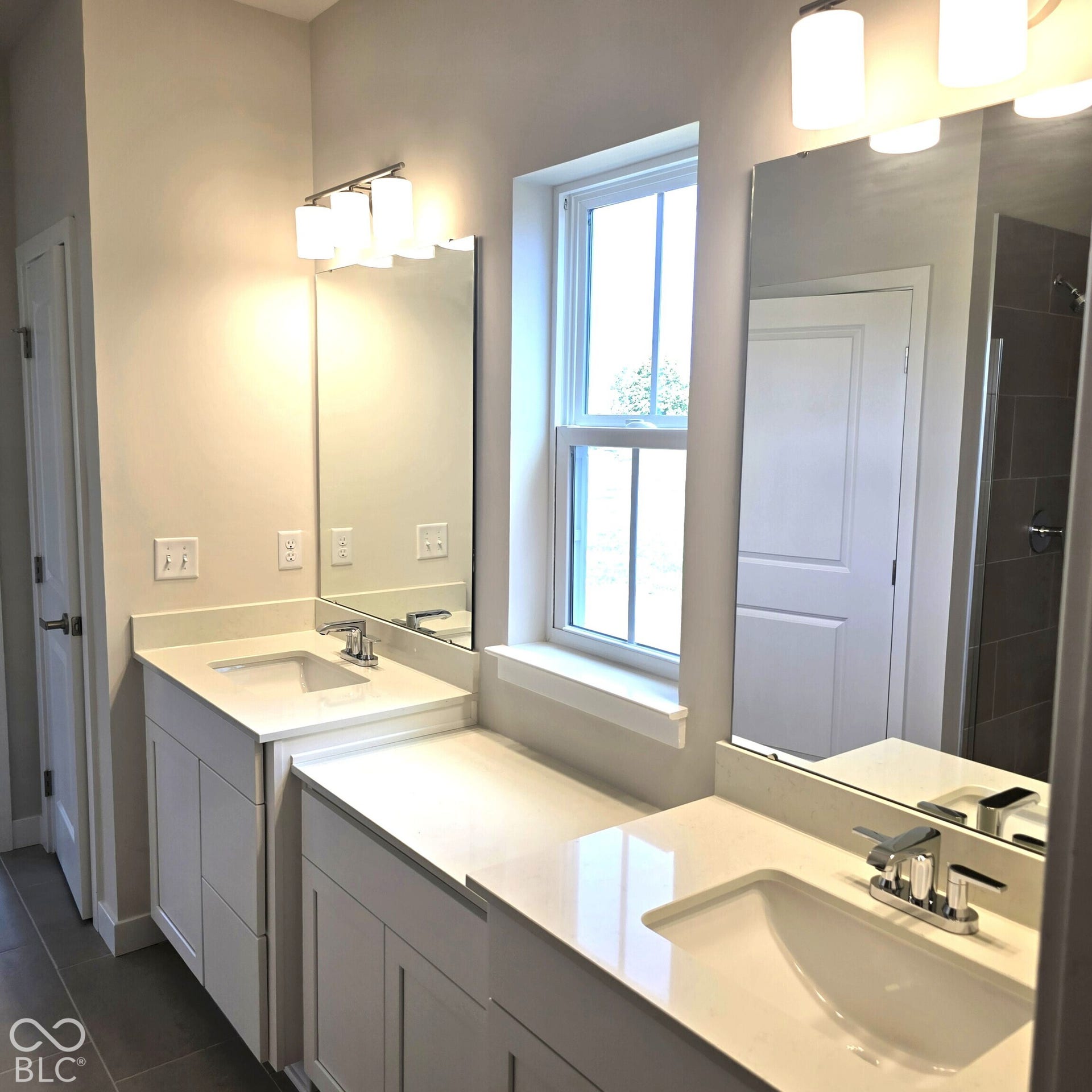 Dual vanities with integrated sinks and chrome fixtures, ample countertop space, contemporary lighting, and a double-hung window