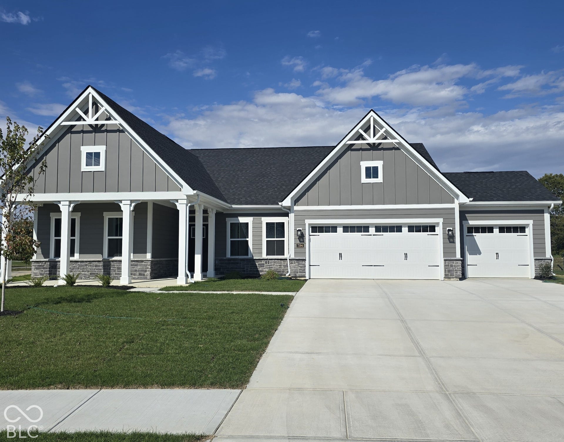 Grey siding exterior with white trim, stone accents, two-car garage, covered entry, and a concrete driveway