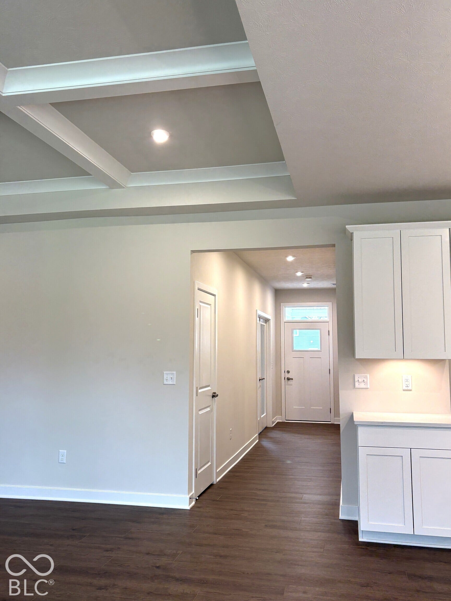 Coffered ceiling with recessed lighting, wood-finish flooring, white shaker cabinetry, and a paneled entry door with transom window