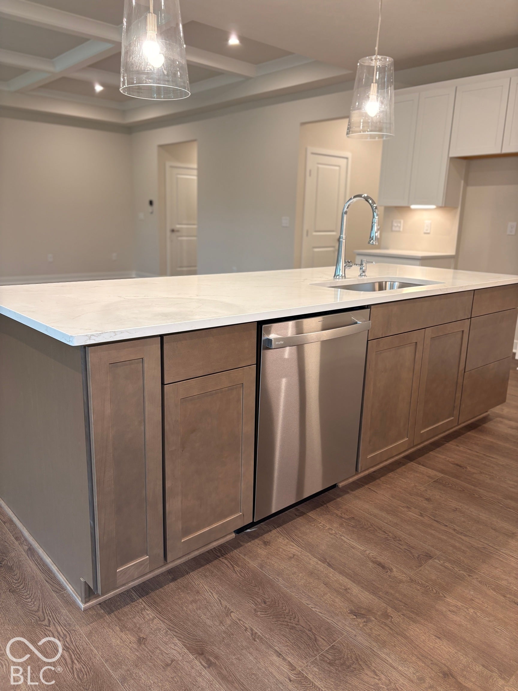 Kitchen island with light-toned countertop, stainless steel dishwasher, and wood-finish flooring