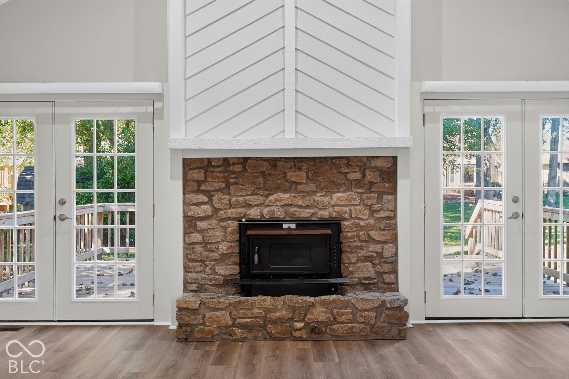 Stone fireplace with an integrated firebox, flanked by French doors with grid-patterned lites, and topped with an angled shiplap accent wall