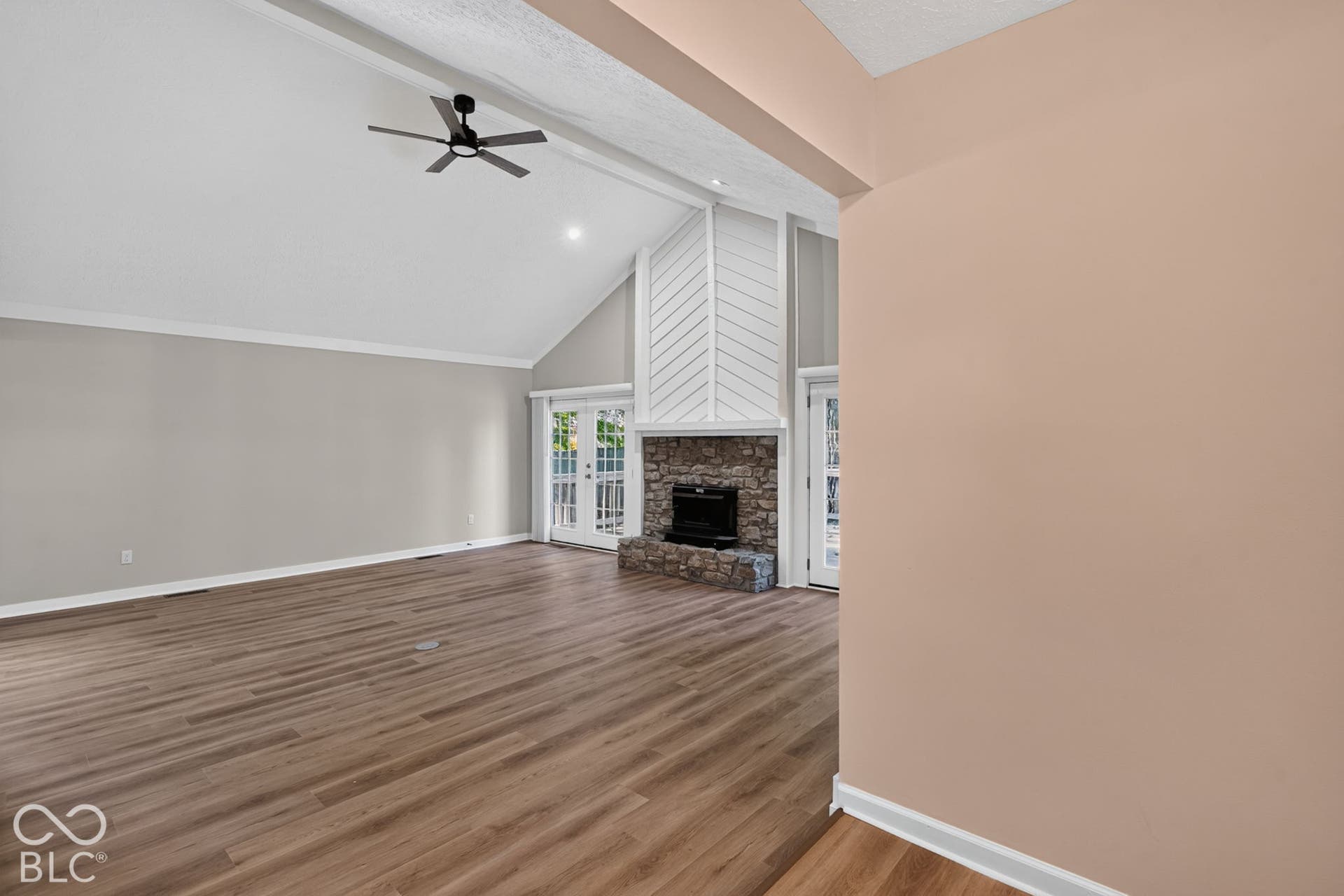 Vaulted ceiling with a ceiling fan, wood-finish flooring, stone fireplace, and double glass-paneled doors