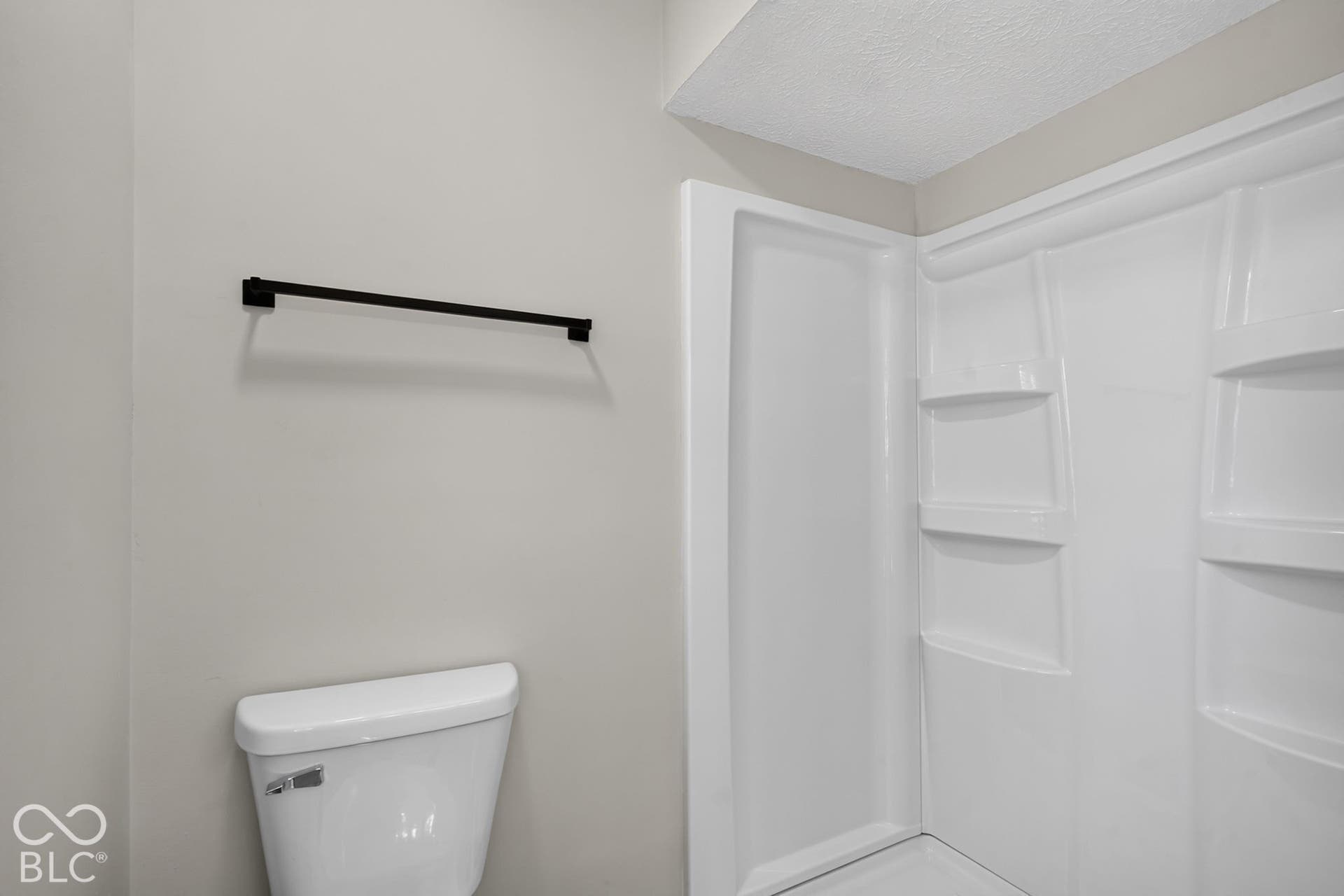 Shower stall with integrated shelving, matte black towel bar, and a white toilet