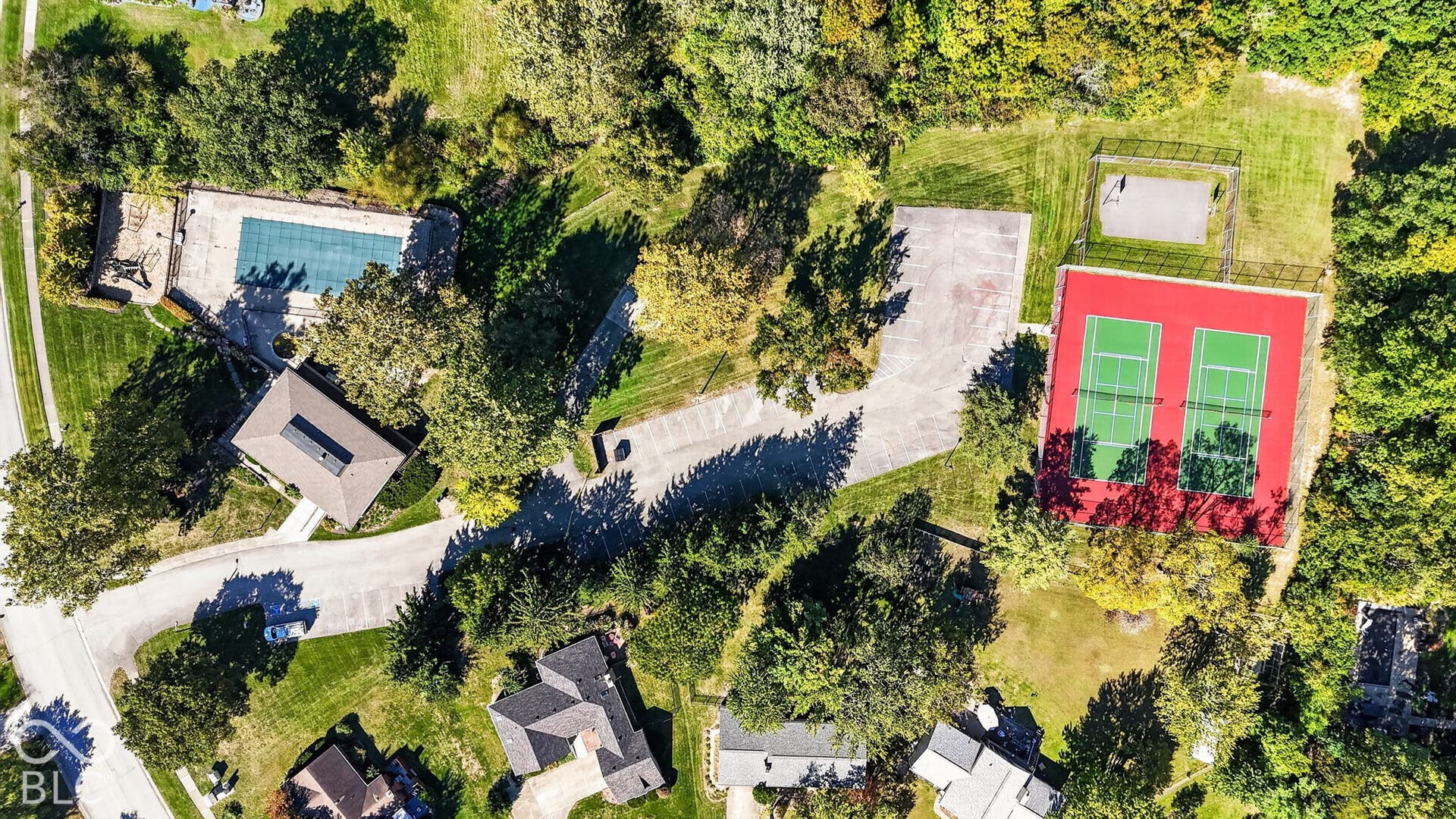 Expansive property featuring a covered outdoor swimming pool, two tennis courts with green playing surfaces, a basketball court, and mature landscaping